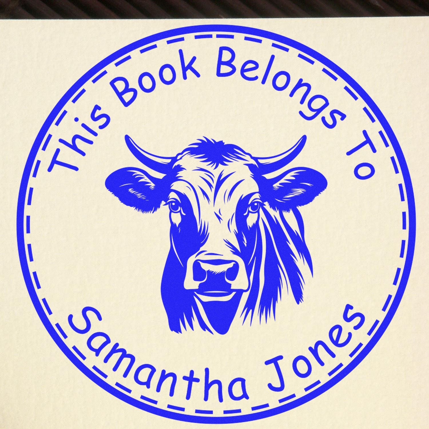 Blue circular book stamp and seal with cow head logo and This Book Belongs To Samantha Jones on cream background