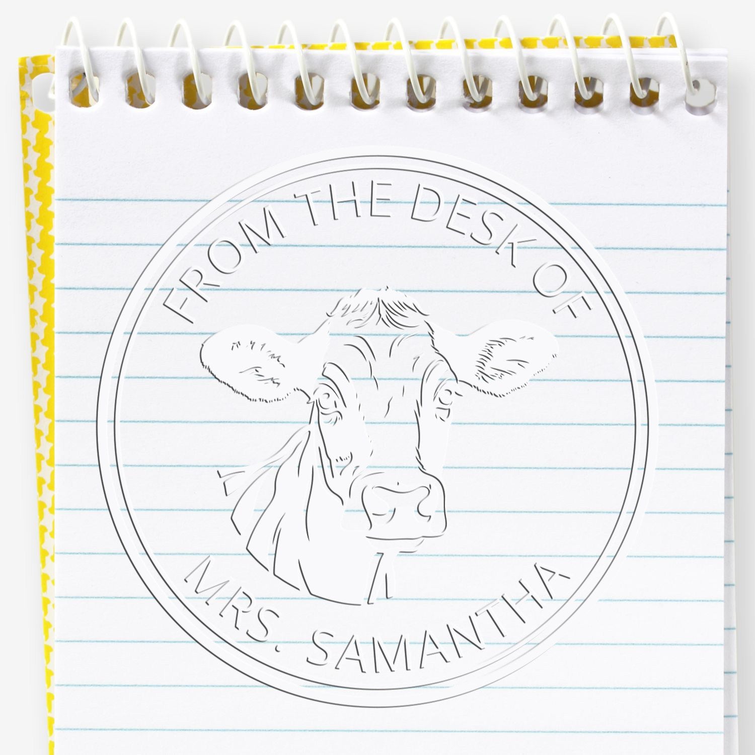 White spiral notebook with an embossed cow desk seal stamp, blue lines, and yellow border; reads Mrs. Samantha.