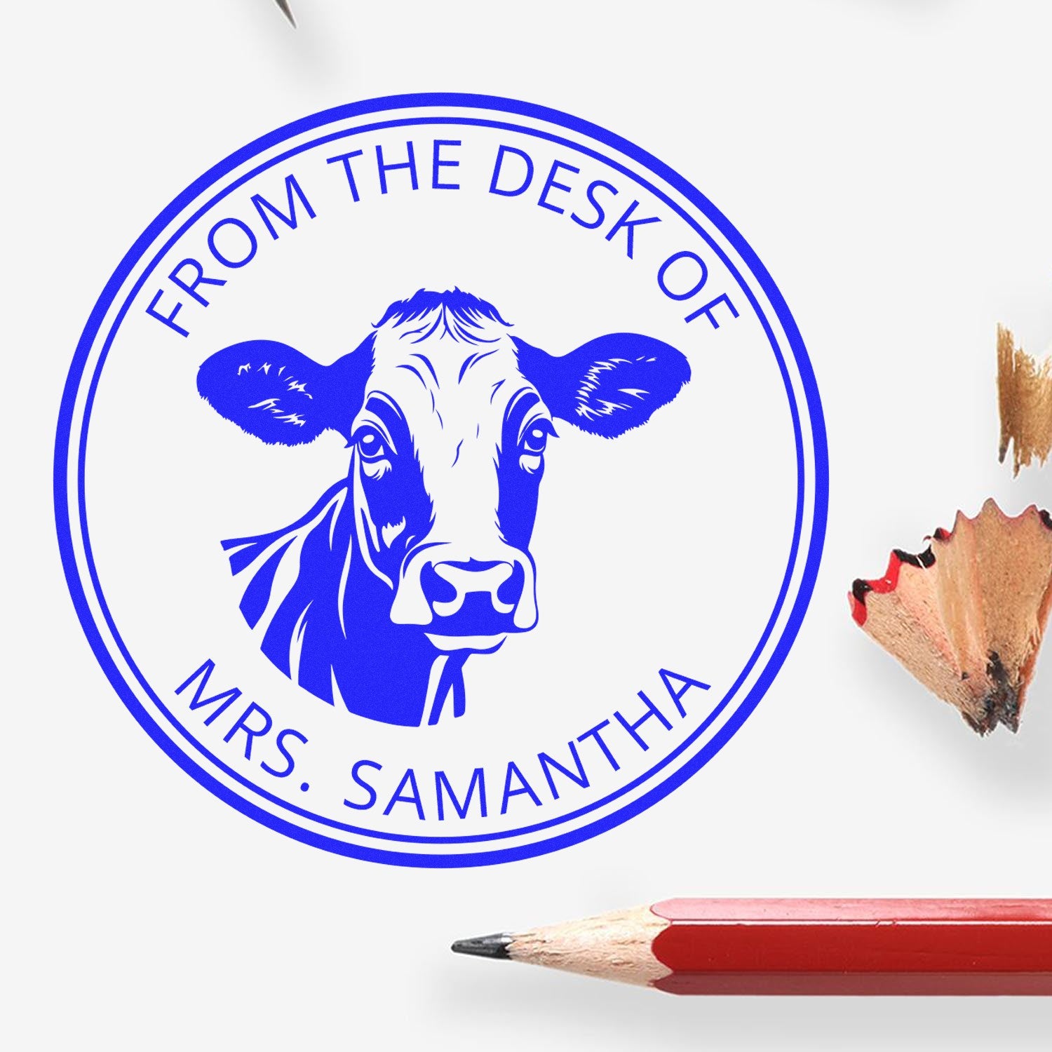 Blue round custom desk stamp seal with cow head and From the Desk of Mrs. Samantha text, shown beside pencil tips.