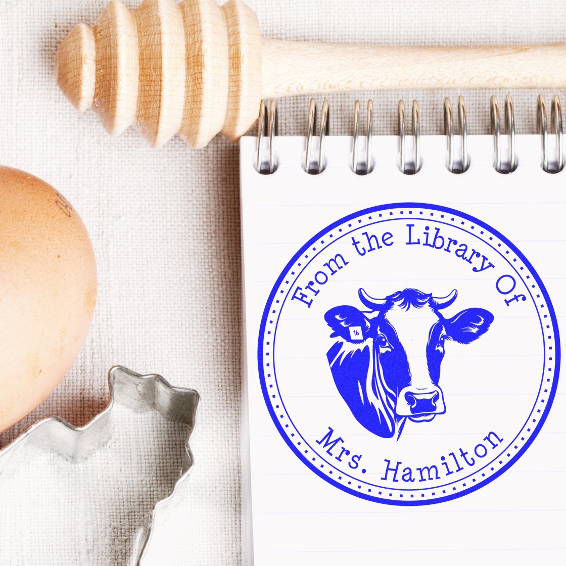Blue custom stamp and seal with cow, From the Library of Mrs. Hamilton, on a notepad beside a wooden-handled stamper.