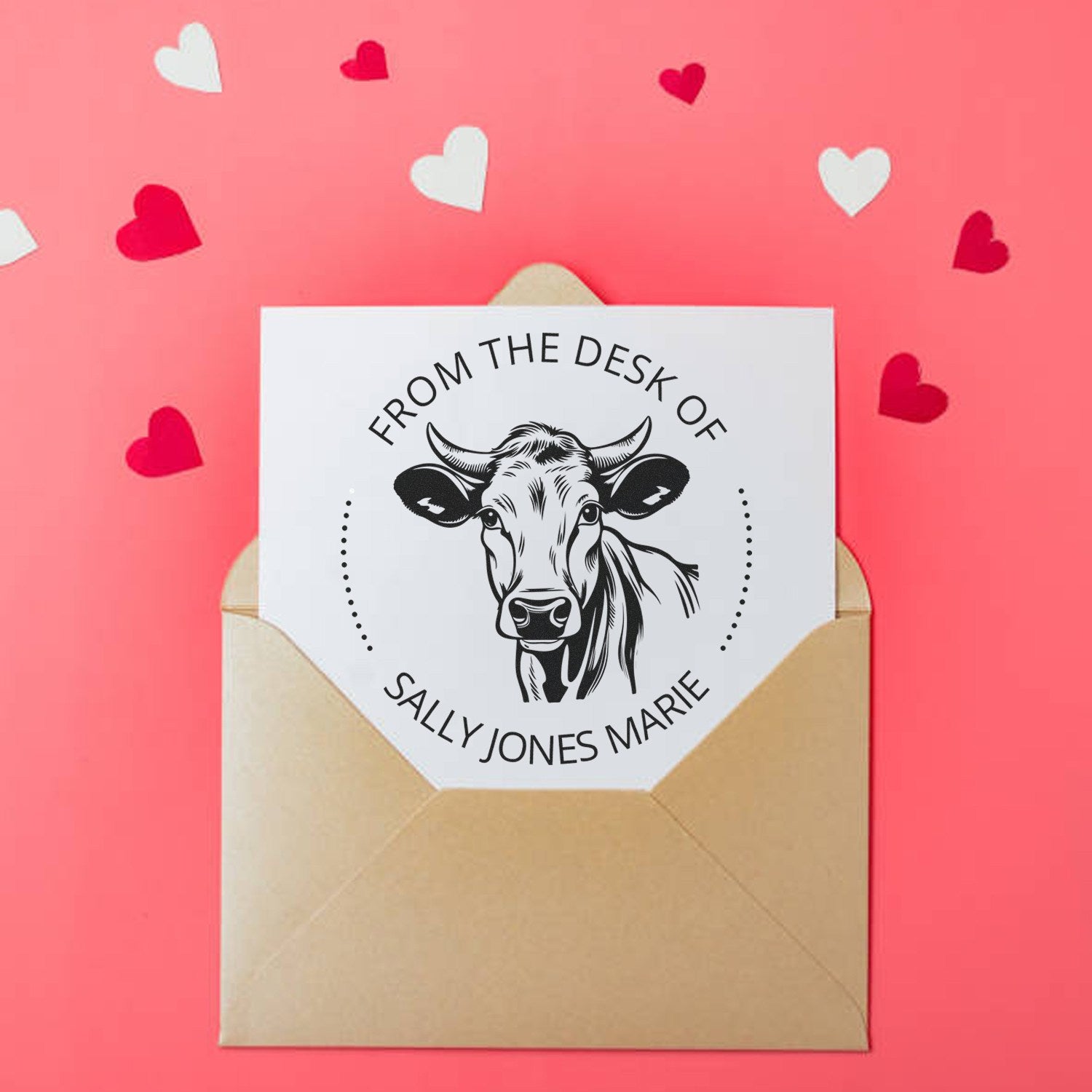 Tan envelope with white custom stamp seal featuring a cow and From the Desk of Sally Jones Marie on pink background with hearts