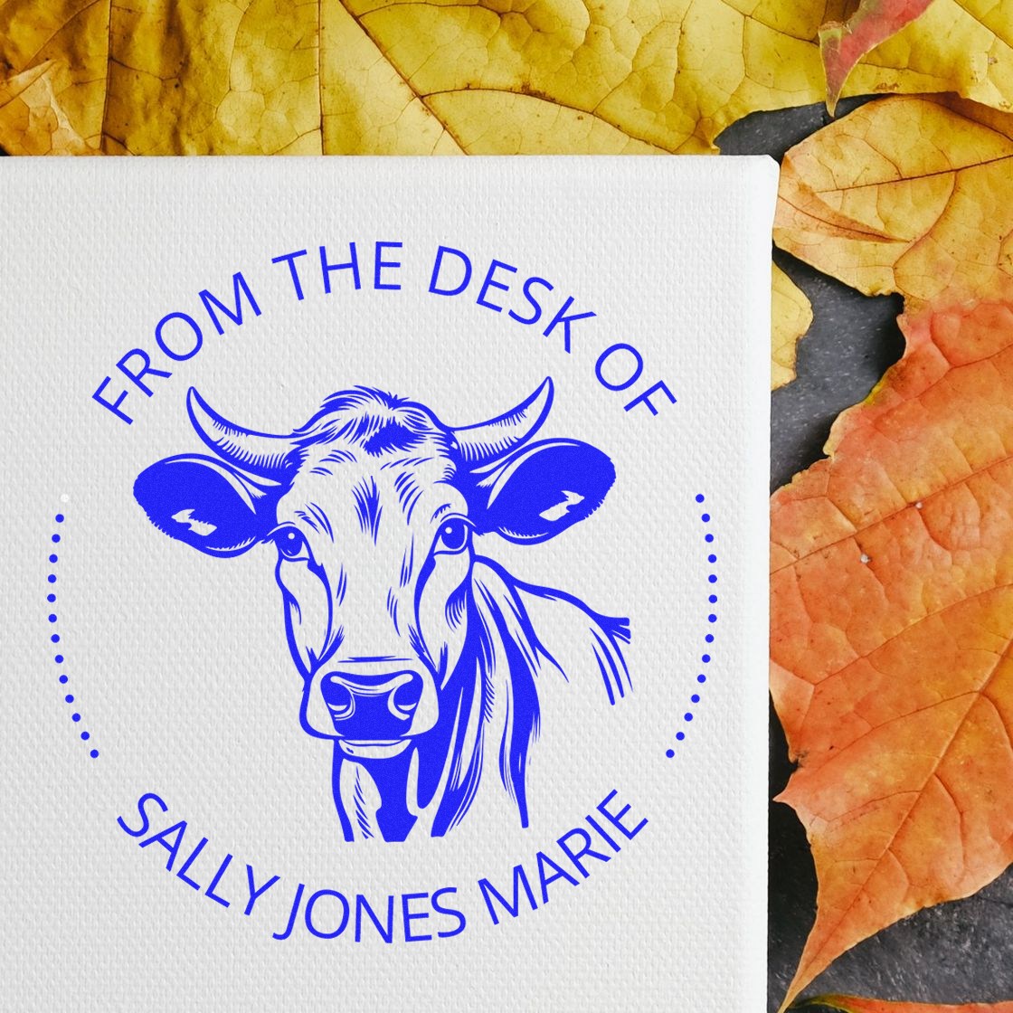 Blue custom stamp and seal with cow head logo and From the Desk of Sally Jones Marie on white, surrounded by autumn leaves.