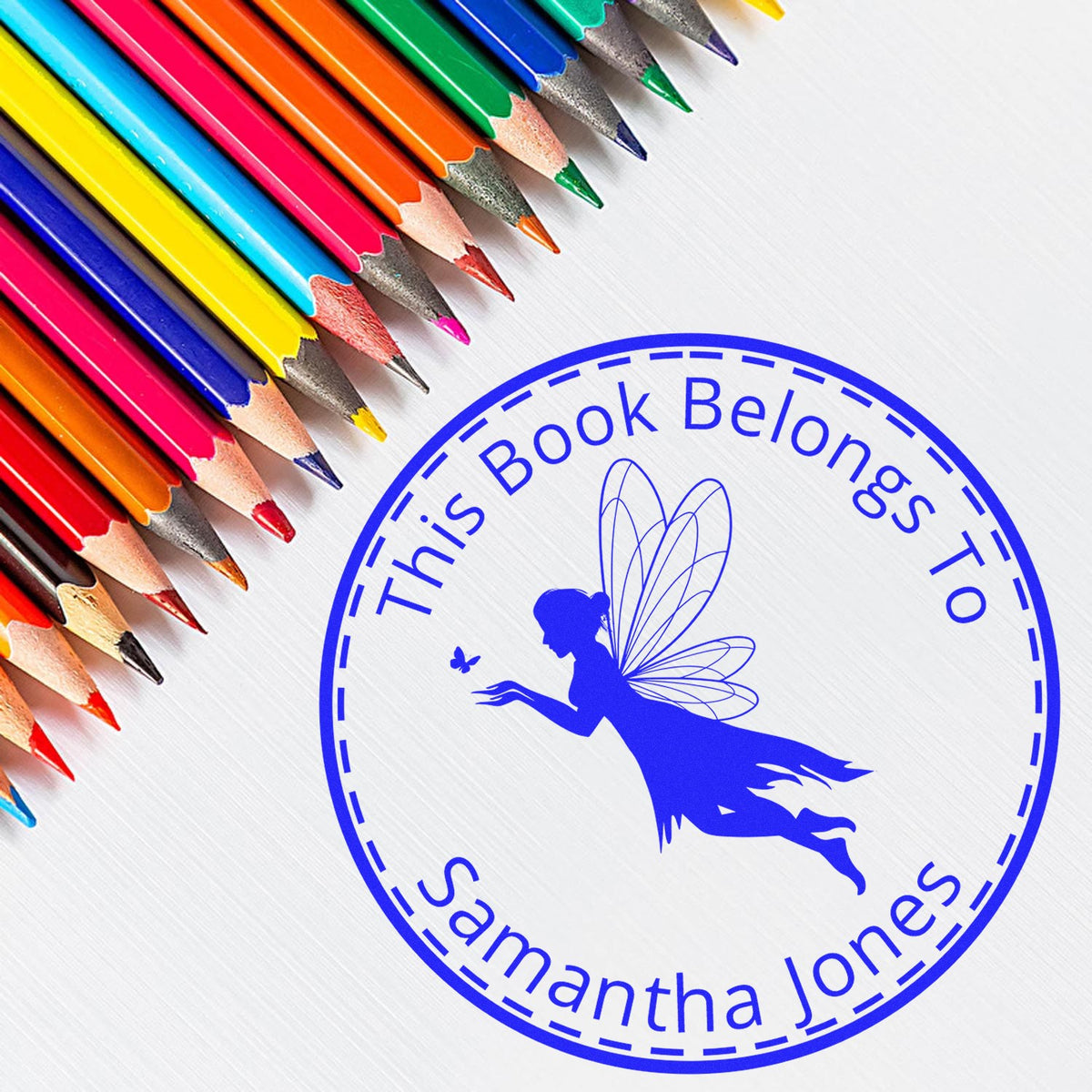 Blue custom book stamp seal with fairy and This Book Belongs To Samantha Jones, beside colorful pencils.