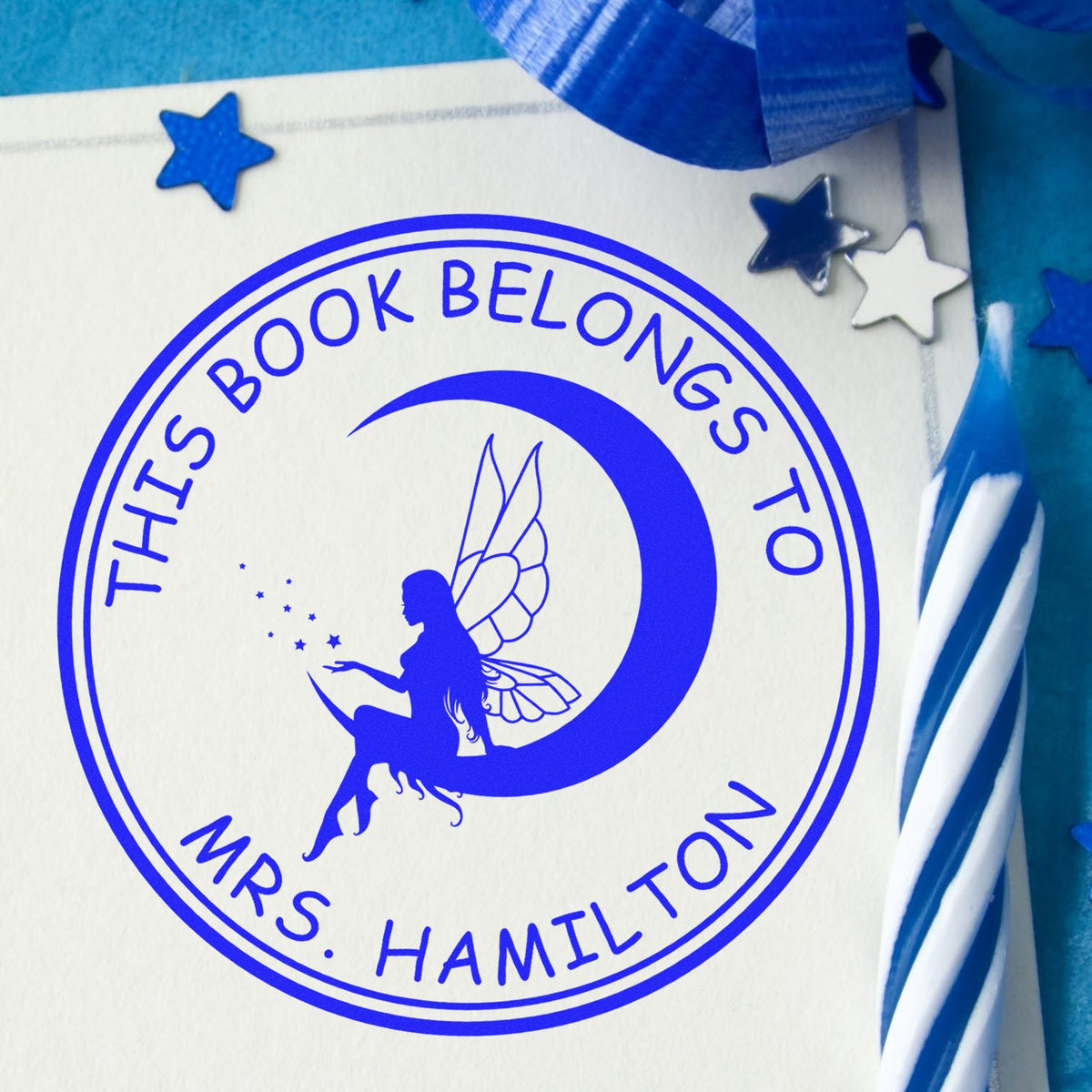 Blue circular book stamp seal with fairy on crescent moon and stars, reading This Book Belongs to Mrs. Hamilton