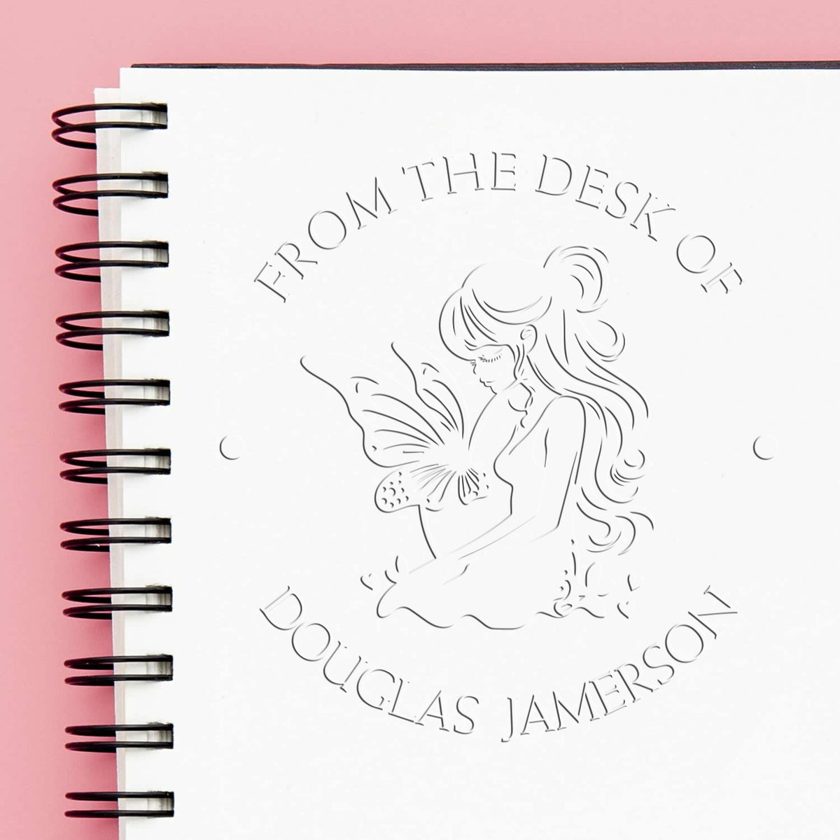 White spiral notebook with embossed desk stamp seal of a girl and butterfly on a pink background