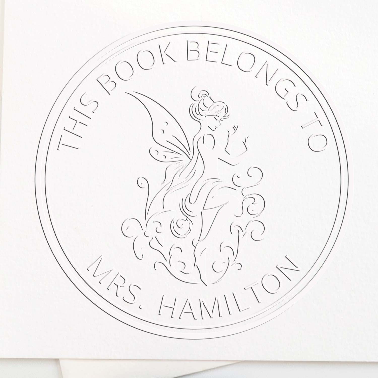 Custom round book embossing seal in white, with fairy design and This Book Belongs to Mrs. Hamilton text.