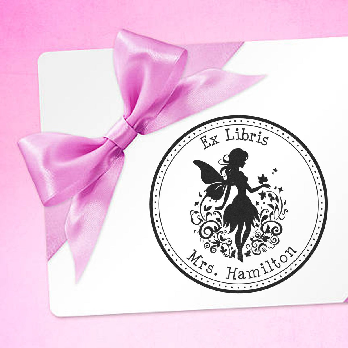 White card with pink satin bow and round black Ex Libris fairy stamp seal reading Mrs. Hamilton