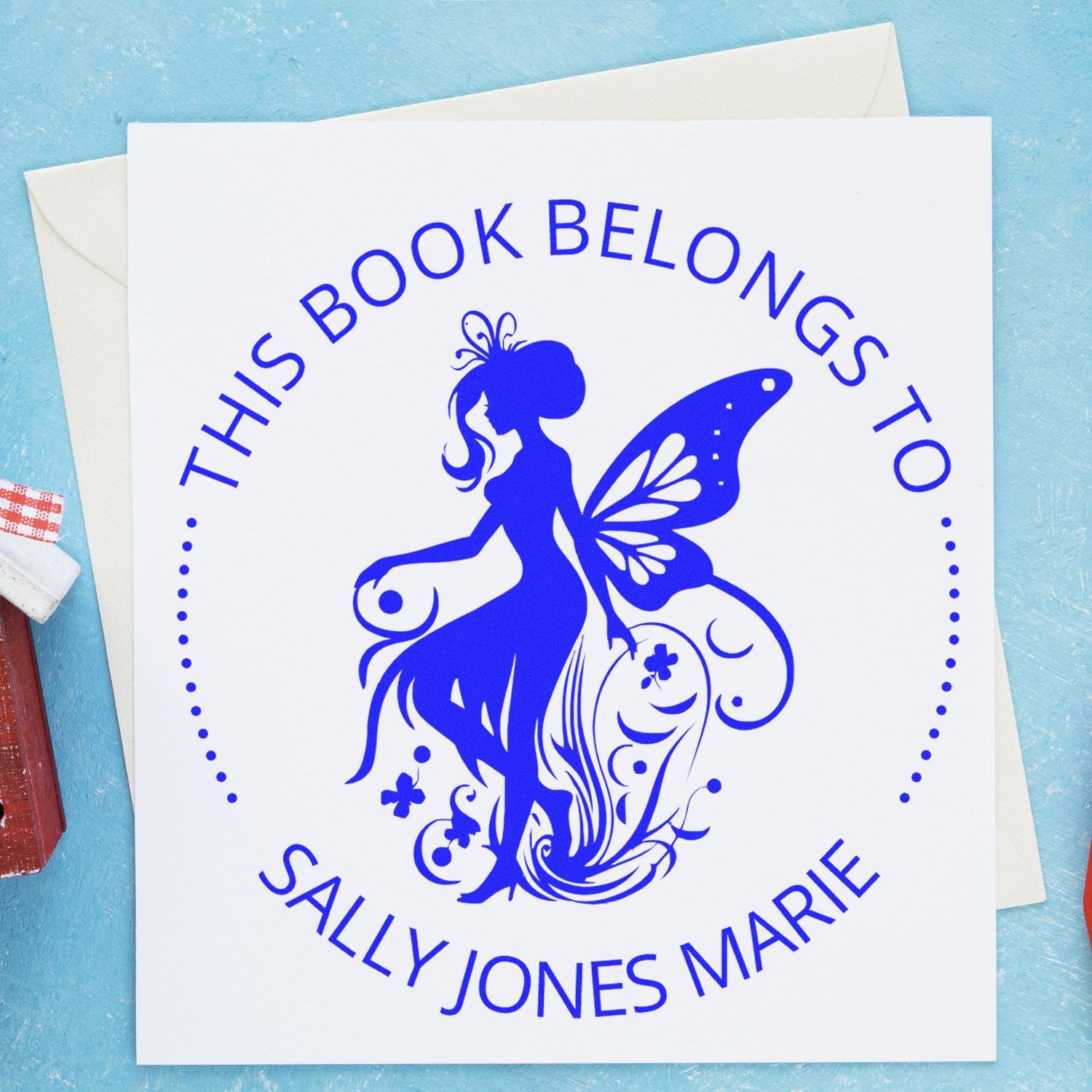 Royal blue custom book stamp and seal with fairy silhouette and This Book Belongs to Sally Jones Marie on white card.