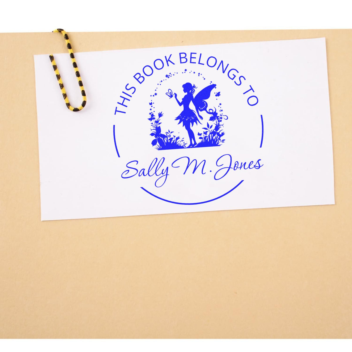 Blue personalized book stamp seal for Sally M. Jones with fairy silhouette on white card, clipped with yellow-black string.