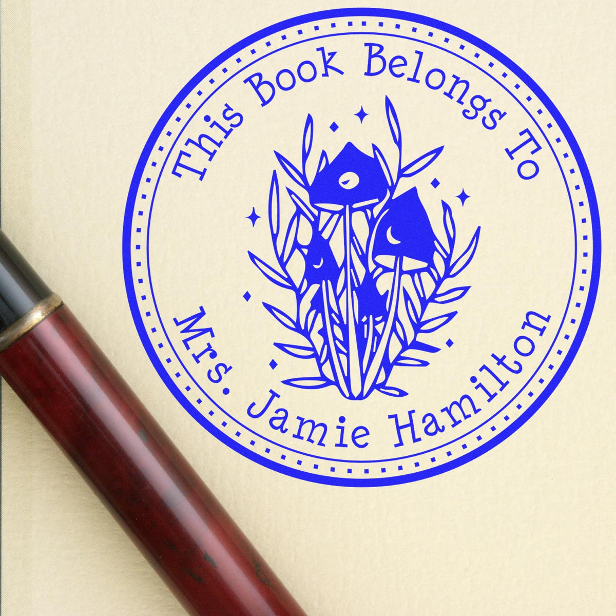 Blue custom bookplate stamp seal with floral design, reading This Book Belongs To Mrs. Jamie Hamilton, on cream paper.