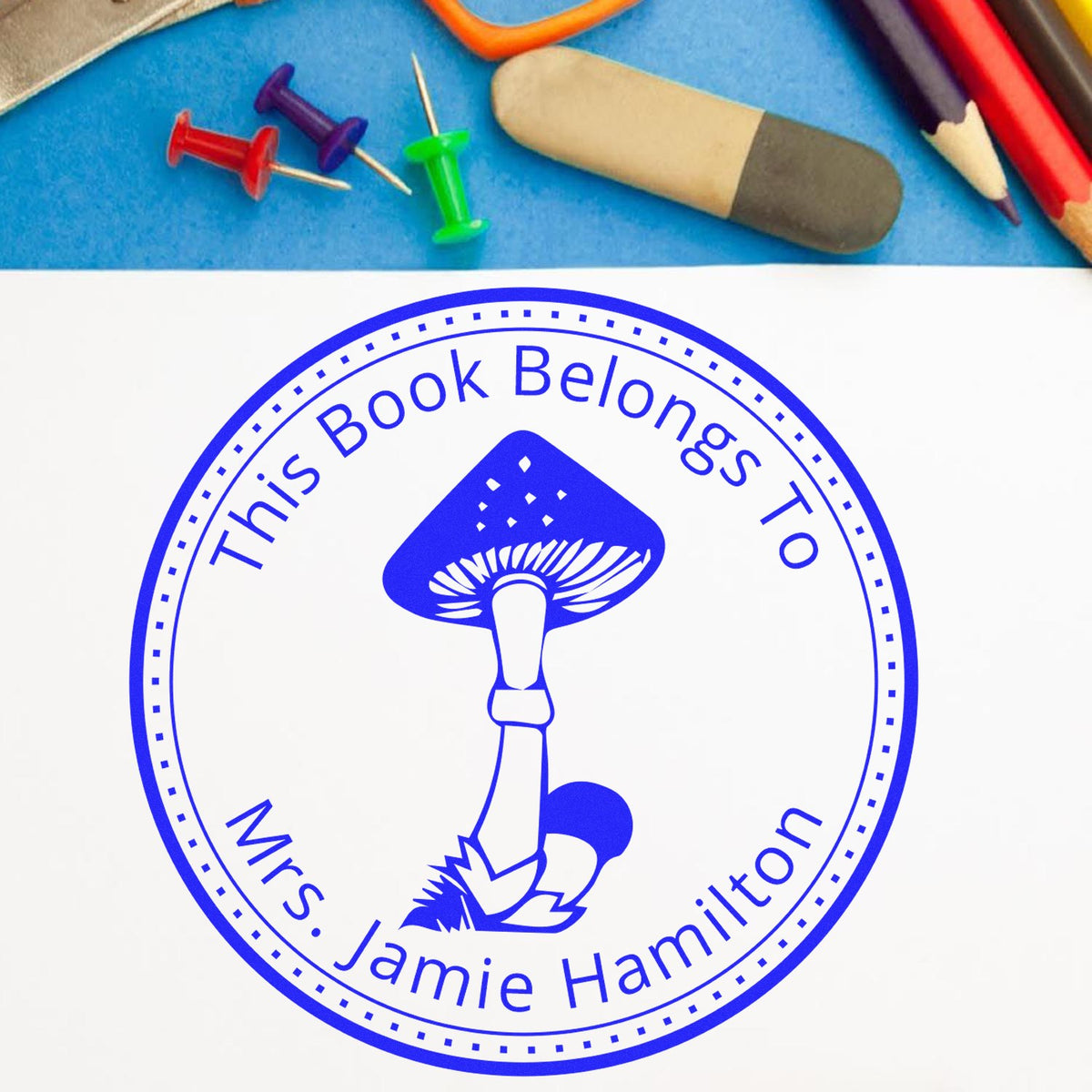 Blue custom book-belongs-to stamp seal with mushroom logo, plus push pins, eraser and colored pencils.