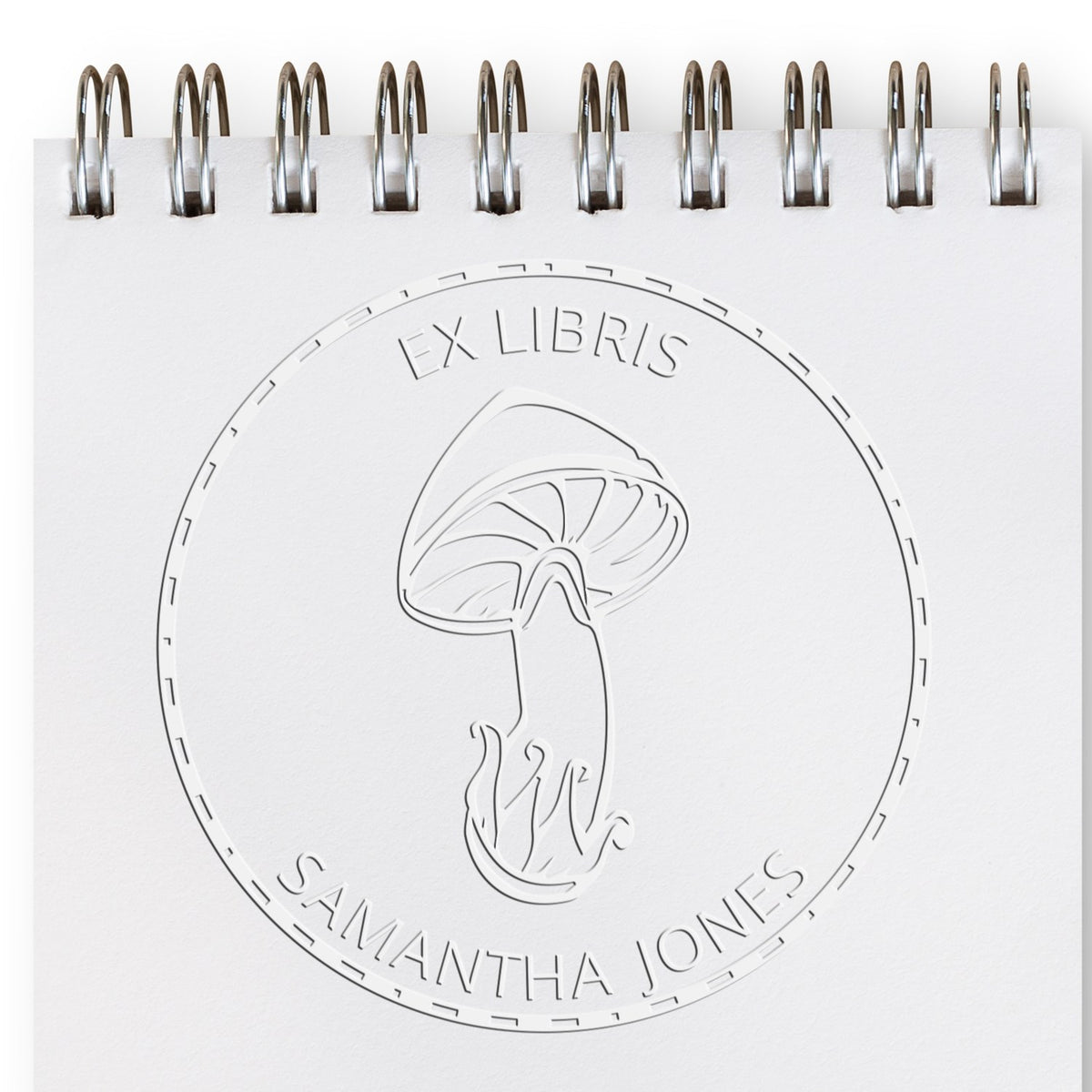 Embossed white ex libris bookplate seal with mushroom logo and Samantha Jones on a spiral-bound page.