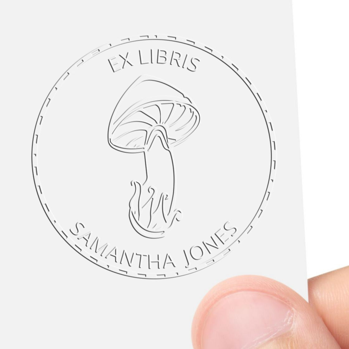 White embossed custom stamp seal with mushroom logo and EX LIBRIS SAMANTHA JONES, held by fingers.