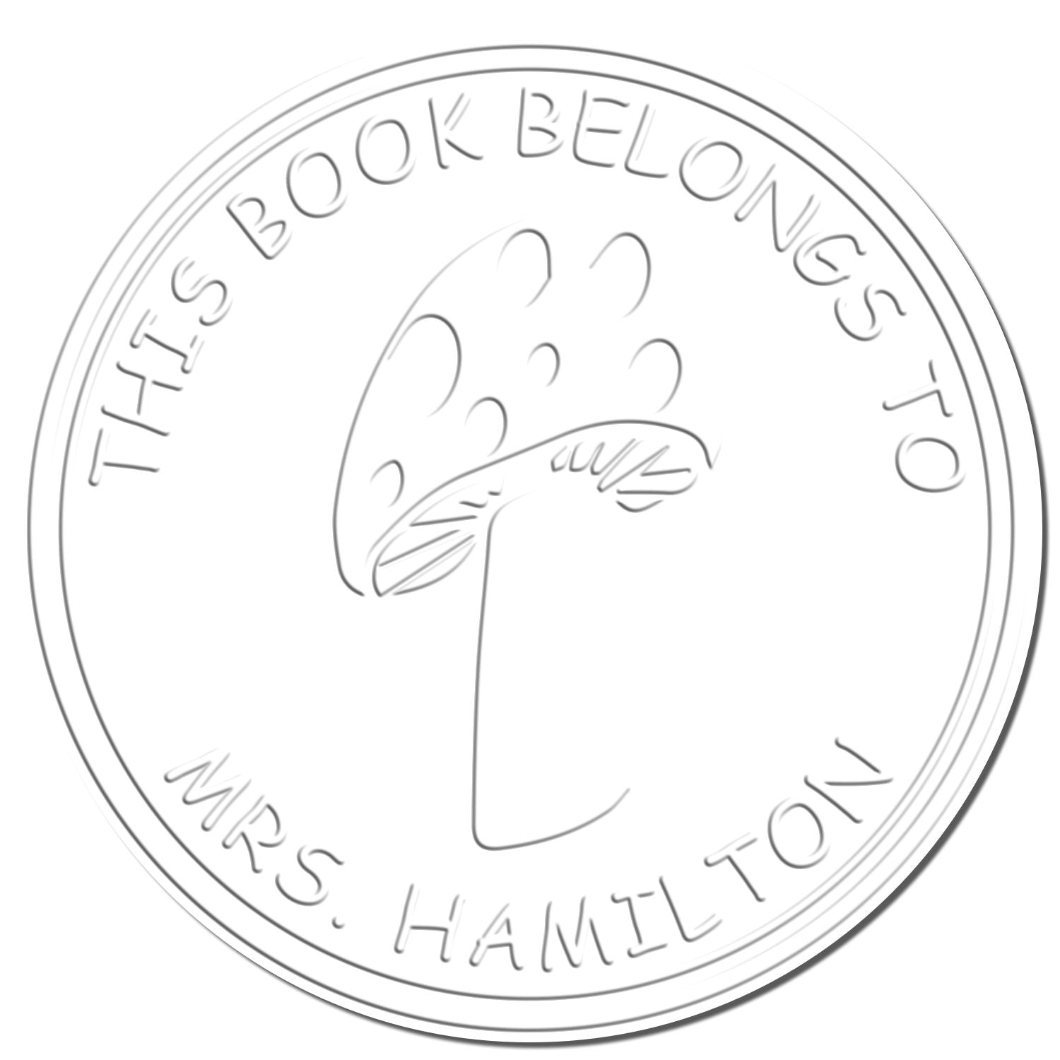 Round silver-gray book stamp seal reading This Book Belongs to Mrs. Hamilton with a hand motif.