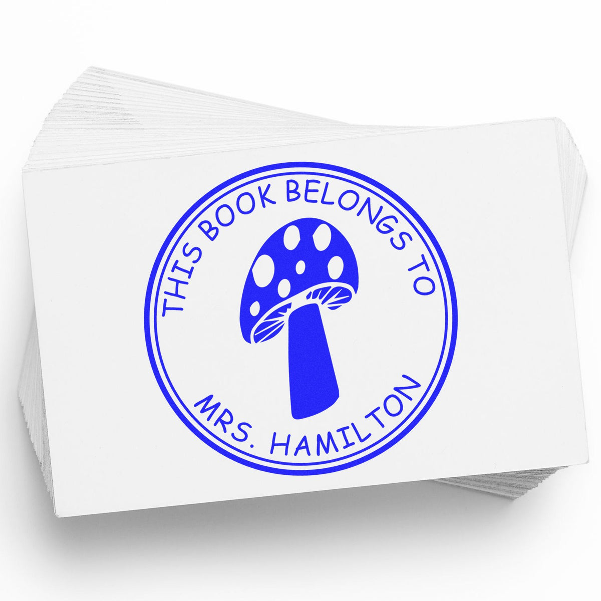 Blue custom book ownership stamp cards with mushroom seal and This book belongs to Mrs. Hamilton on white paper.