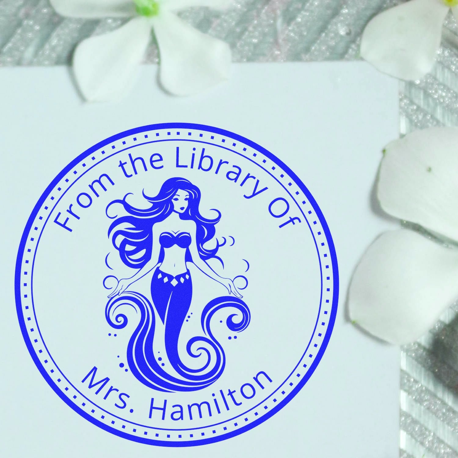 Blue circular library stamp seal with mermaid design reading From the Library of Mrs. Hamilton on white paper.