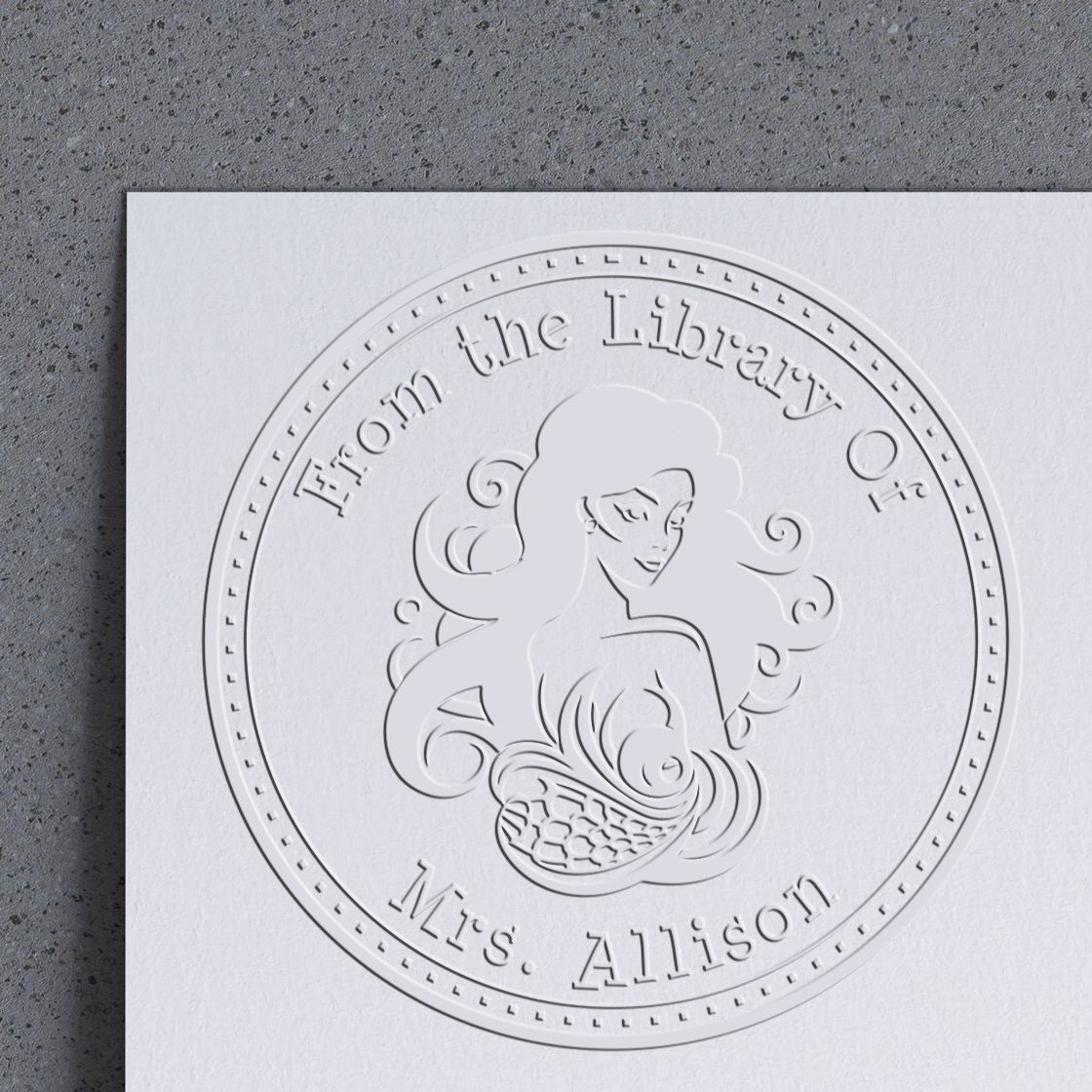 Embossed white circular stamp seal on white paper with mermaid illustration and From the Library of Mrs. Allison text.