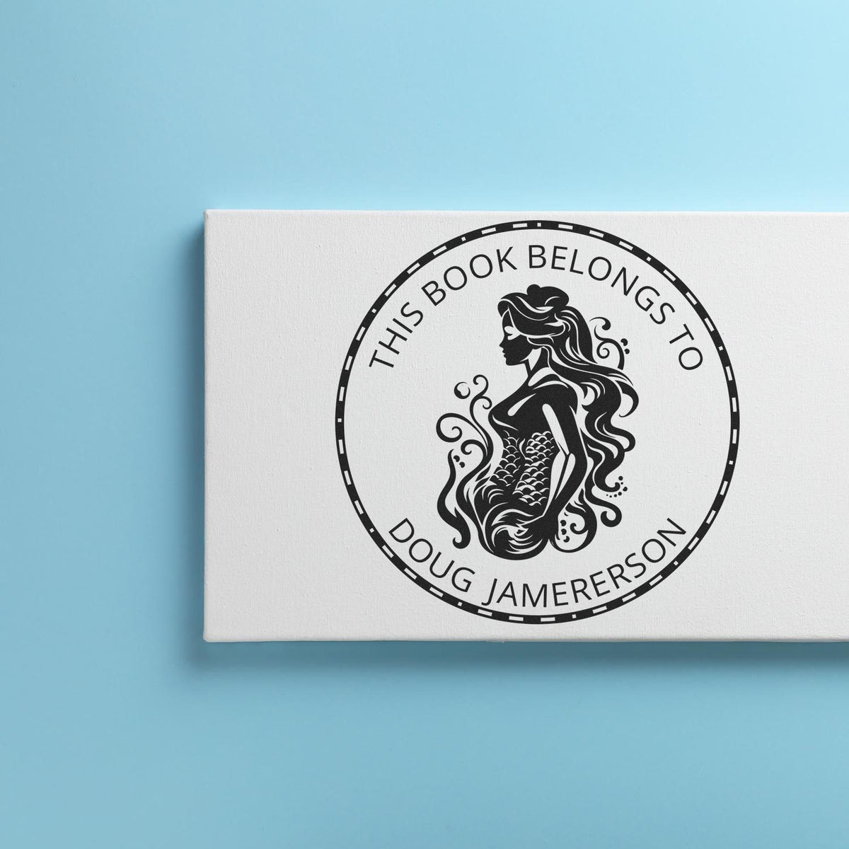 White custom book stamp seal with black mermaid design, This Book Belongs to Doug Jamerson, on light blue background.