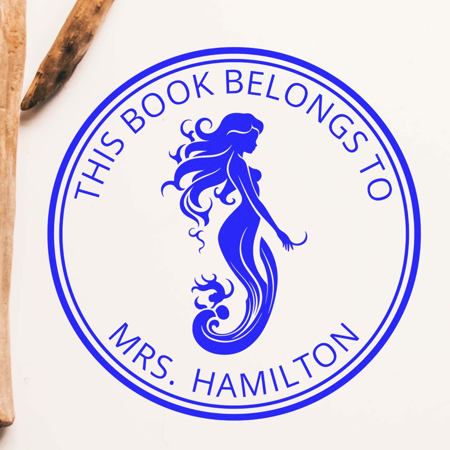 Blue circular stamp seal with mermaid silhouette and This Book Belongs to Mrs. Hamilton text on white background.