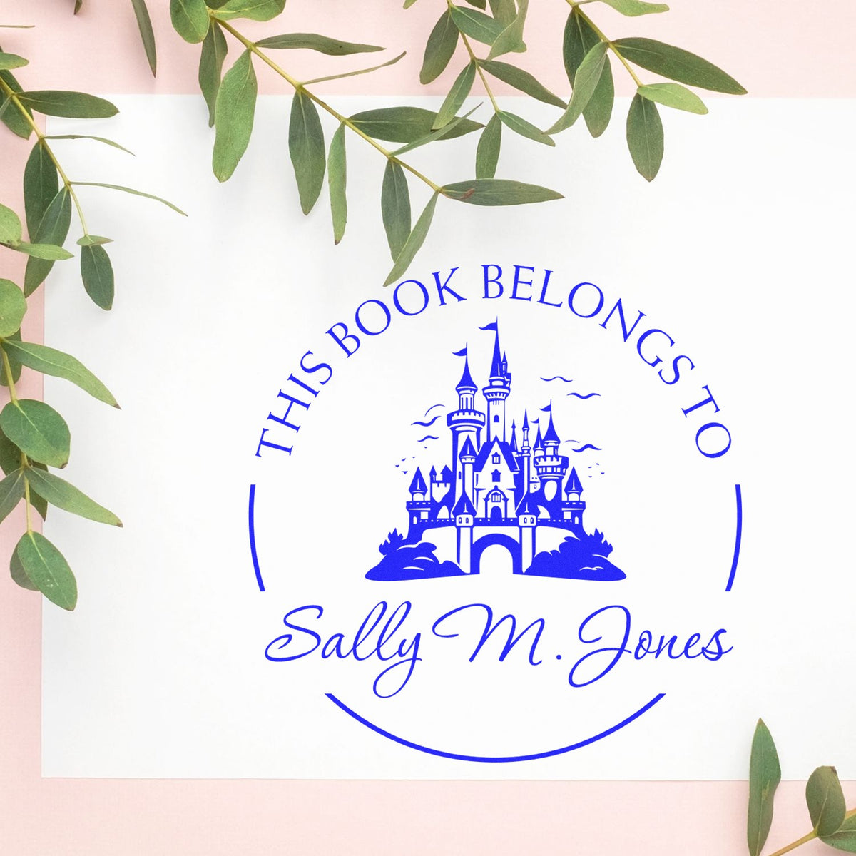 Blue circular book stamp seal with castle emblem, This Book Belongs To, and Sally M. Jones, on white with green leaves.