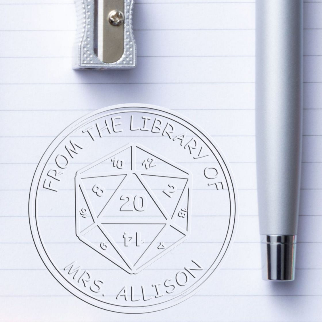 Silver library stamp seal on lined paper, reading From the Library of Mrs. Allison with geometric dice design.