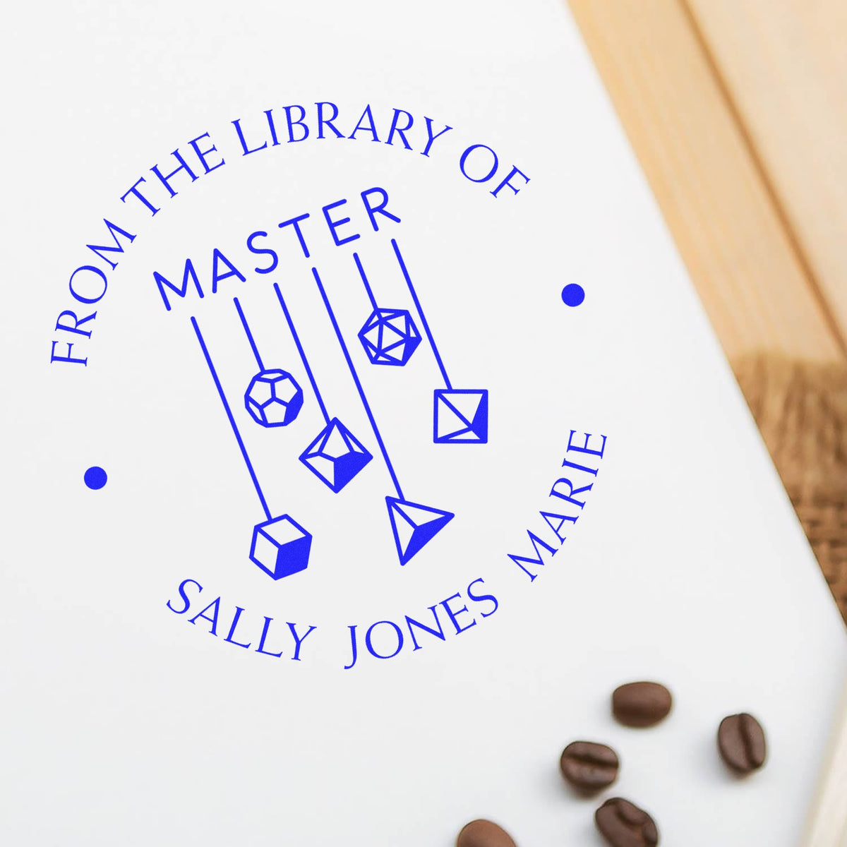 Blue custom library stamp seal with geometric pendants, reading From the Library of Master Sally Jones Marie, on white paper.