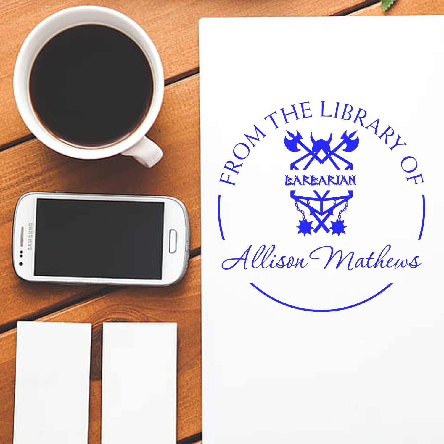 Blue custom stamp and seal design on white paper with swords emblem and Allison Mathews, beside coffee and phone.
