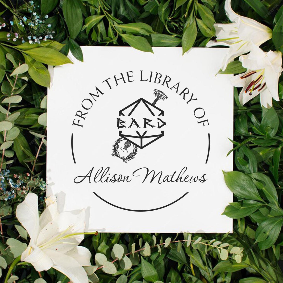Custom black library stamp and seal for Allison Mathews on white card, framed by green leaves and white lilies.