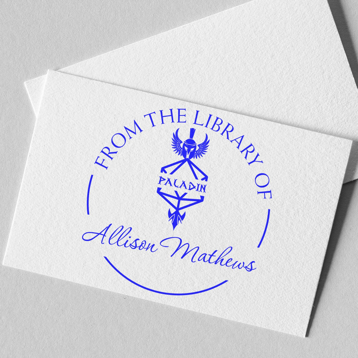 White paper cards with blue custom library stamp seal reading From the Library of Allison Mathews and winged emblem.