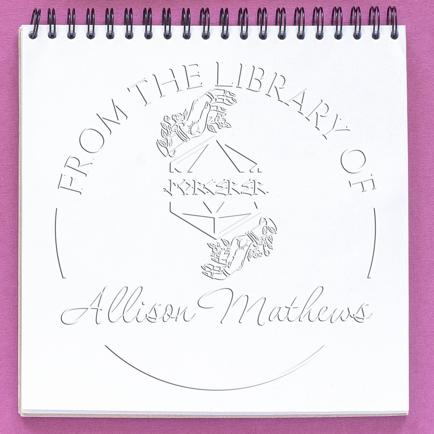 White spiral notebook with embossed library stamp and seal for Allison Matthews on a purple background.