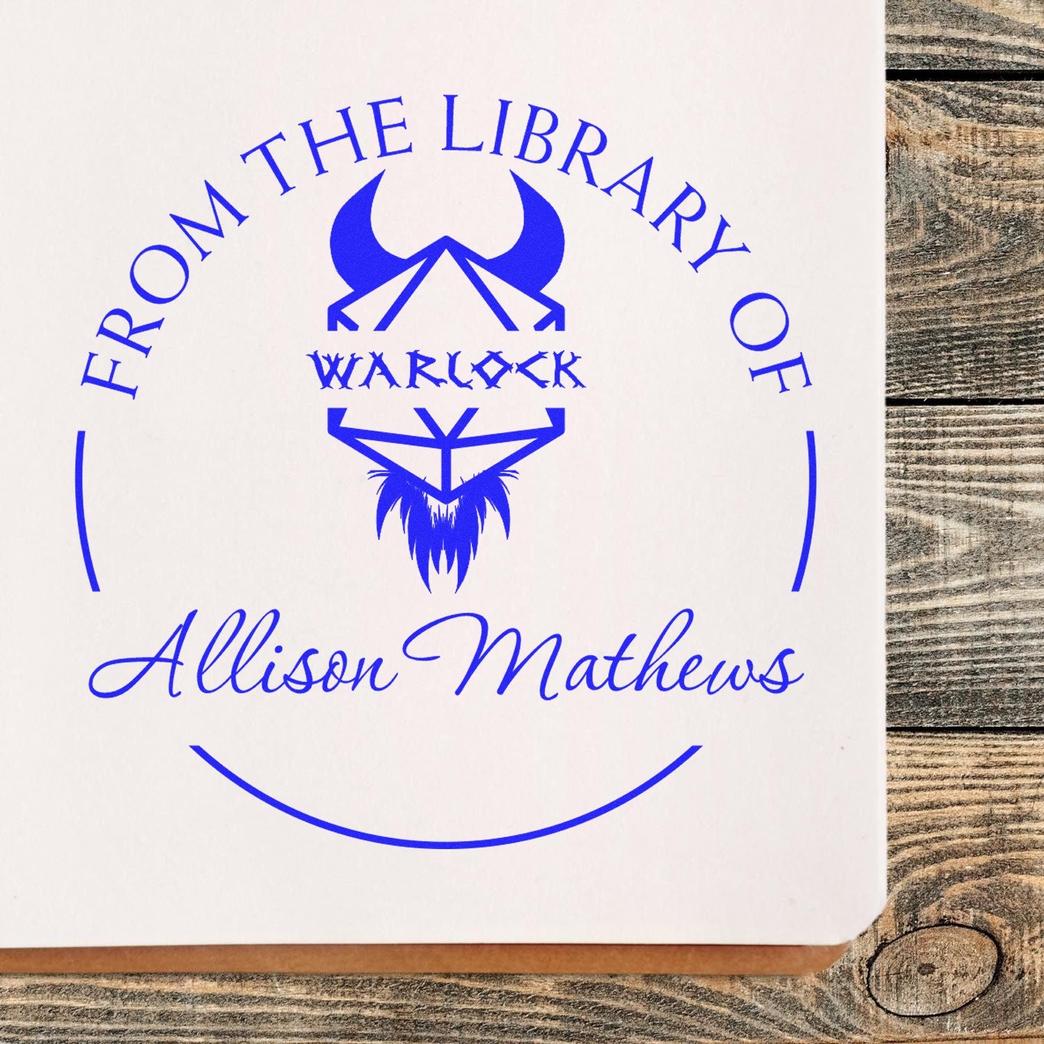 Blue custom library stamp seal with From the Library of, wolf logo, and Allison Mathews on white paper.