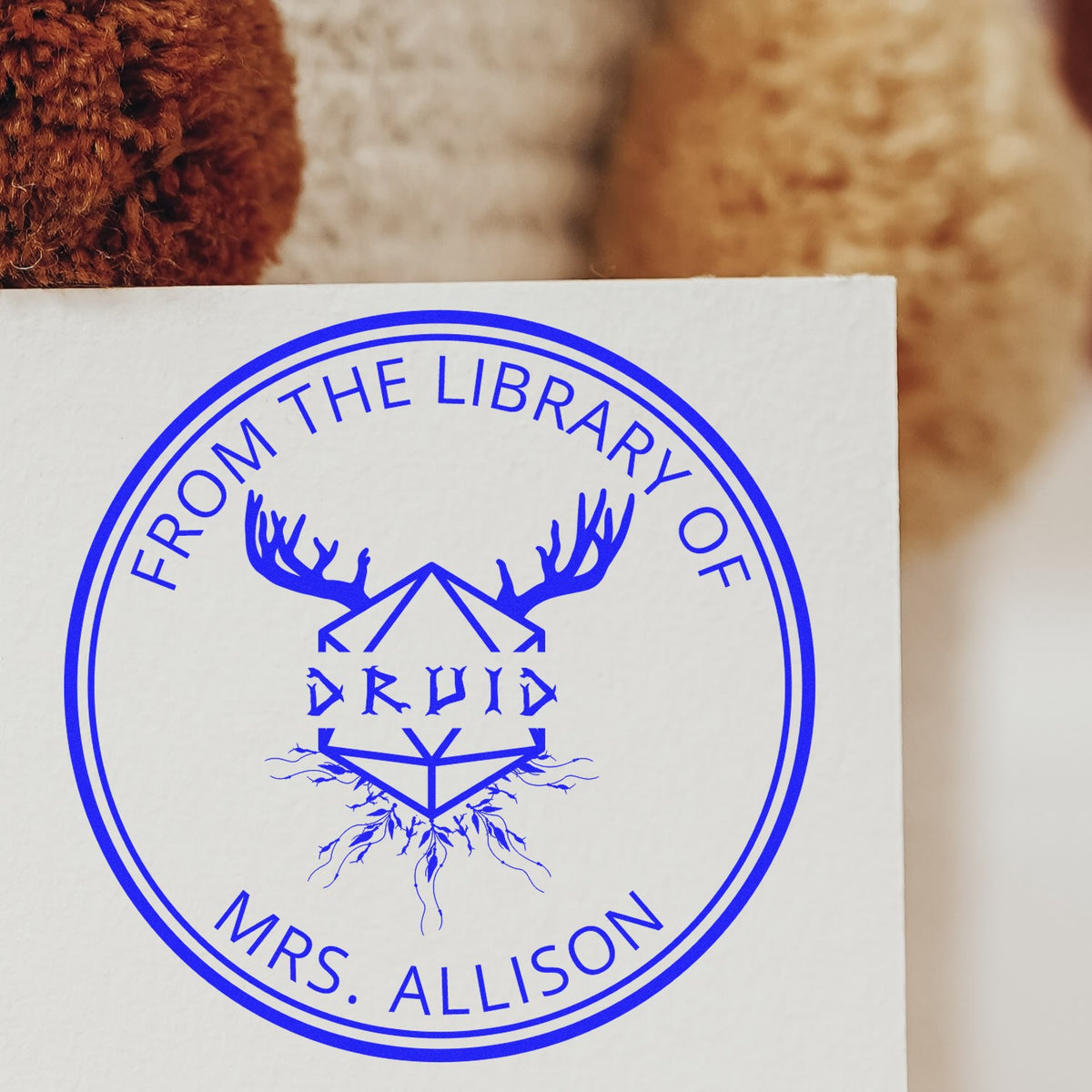 Blue circular custom stamp seal on white paper, reading From the Library of Druids and Mrs. Allison, with antlers and geometric design.