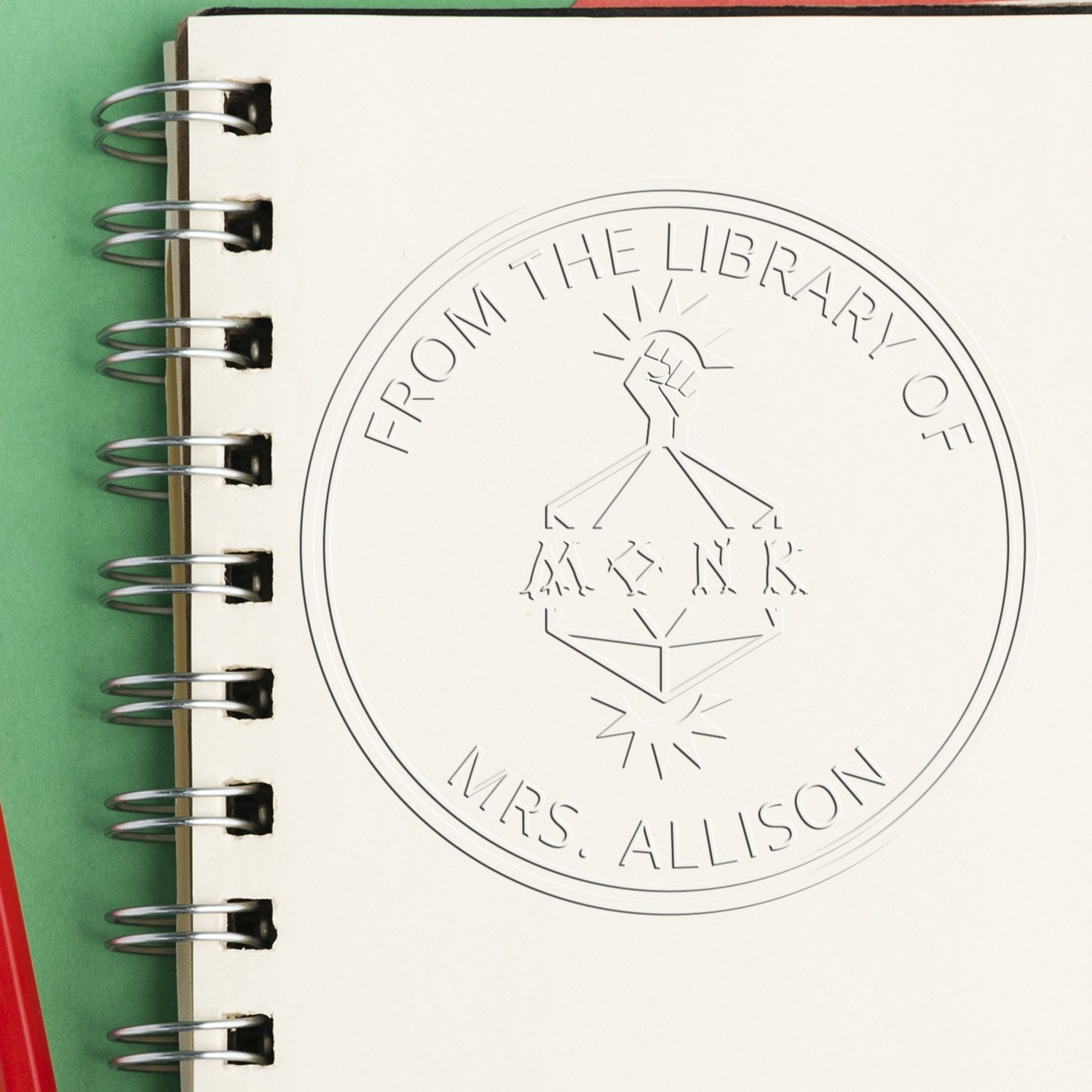 Cream spiral notebook with custom embossed library seal reading ĀFrom the Library of Mrs. AllisonĀ on green background.
