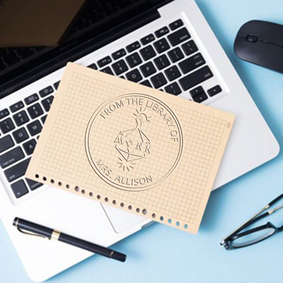 Custom stamp and embossed seal on beige grid paper over a laptop keyboard, with black pen, mouse and glasses on a blue desk.