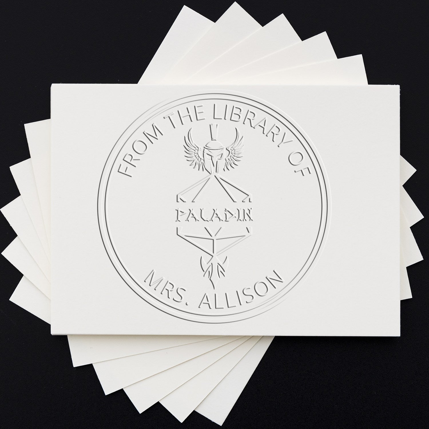 White embossed custom stamp seals on a black background, featuring a circular emblem with wings and text.