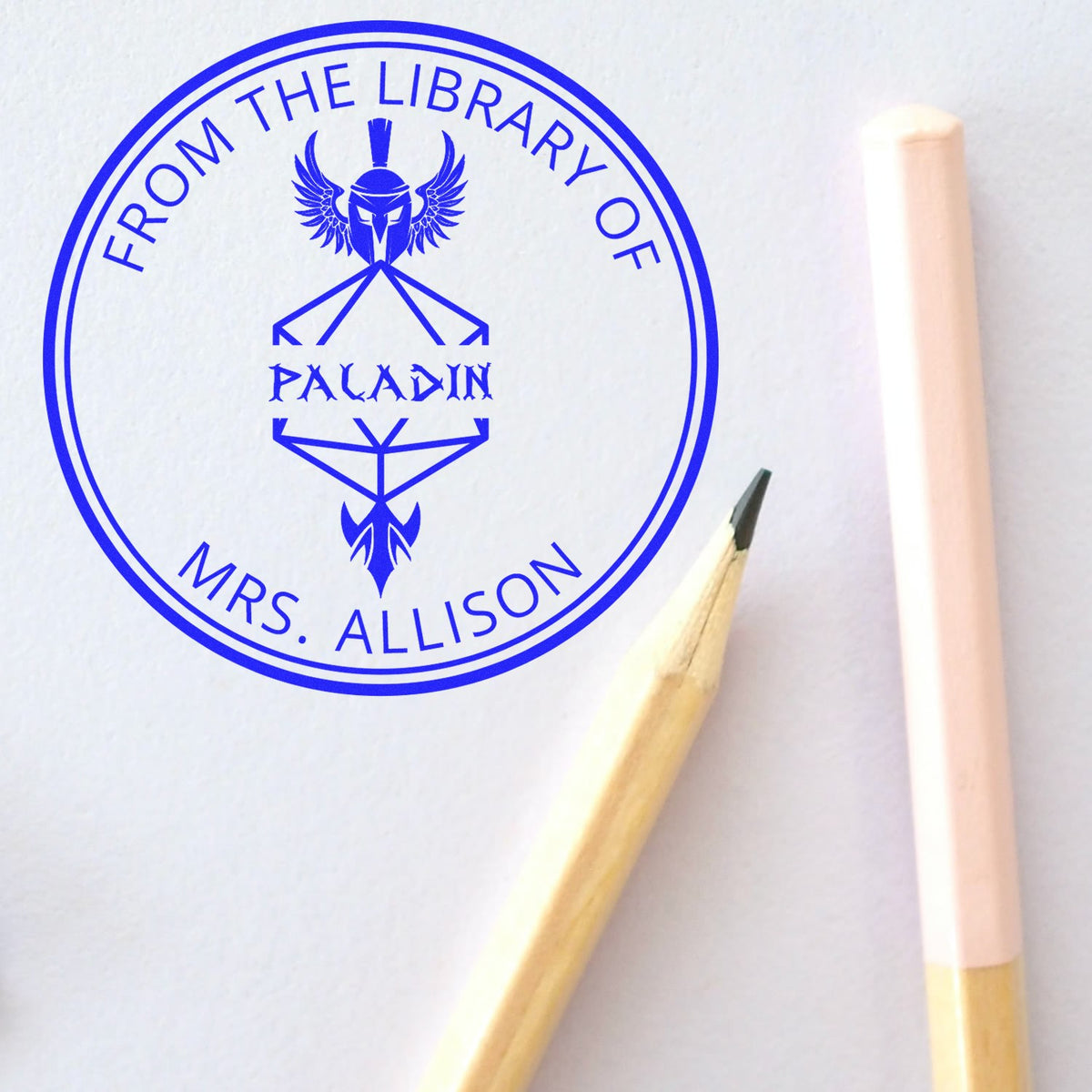 Blue custom stamp seal reading From the Library of Paladin Mrs. Allison with a winged emblem on white paper.