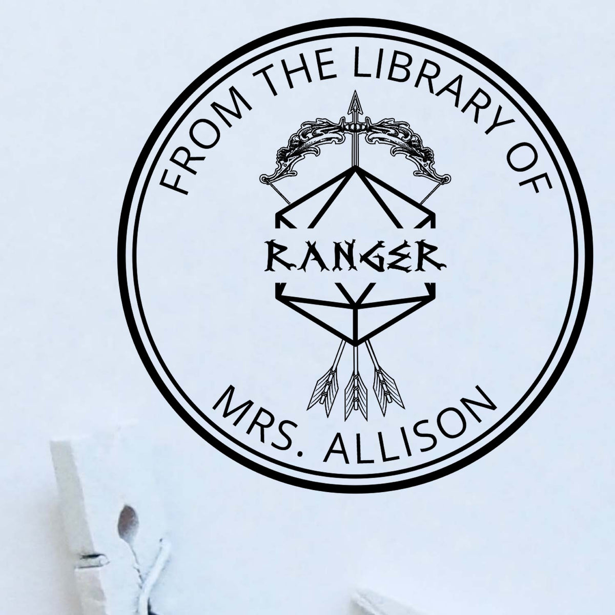 Black round library stamp seal with dreamcatcher and arrow design, reading From the Library of Ranger Mrs. Allison.