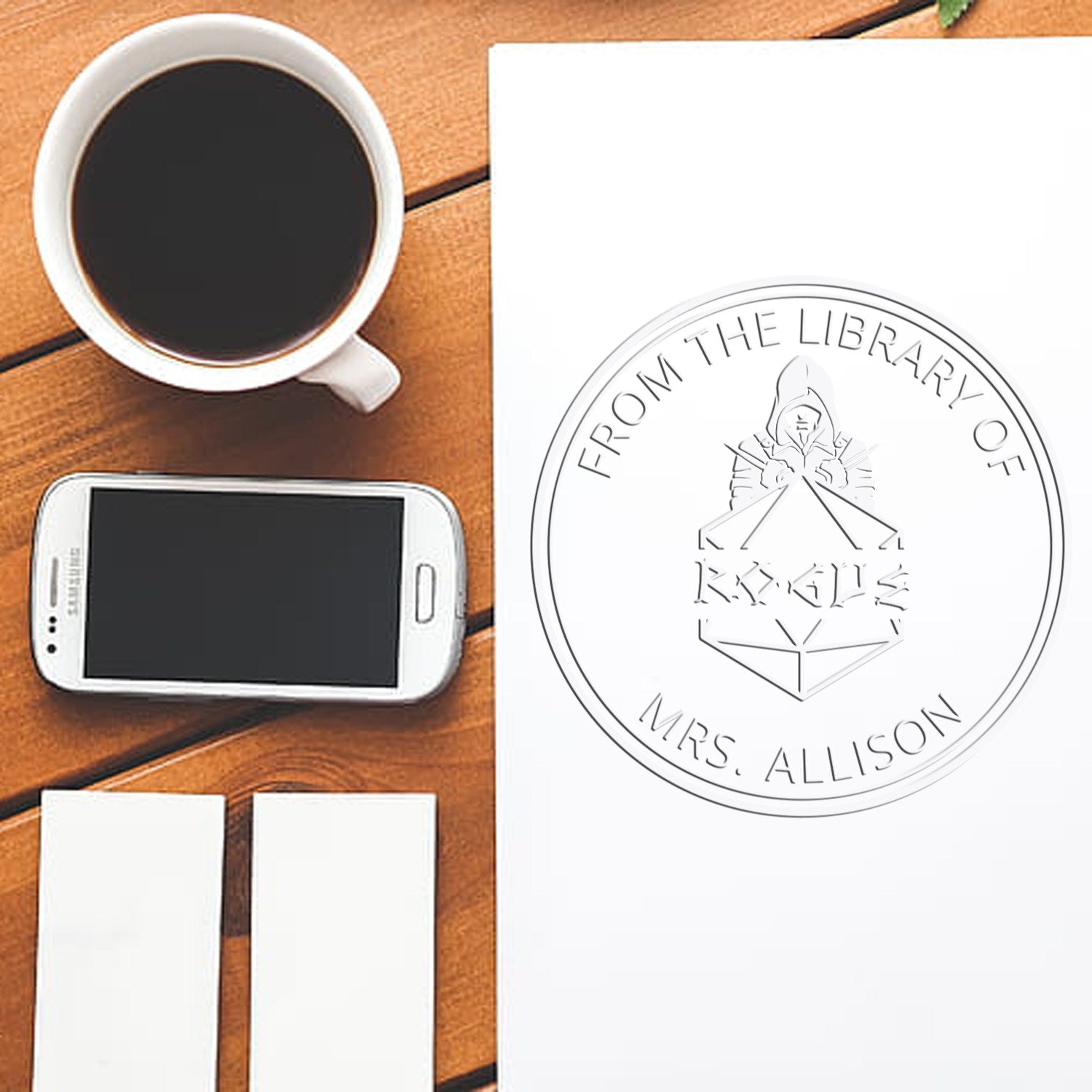 Custom library stamp and seal set with white circular bookplate, coffee cup, smartphone, and blank labels on a wooden table.