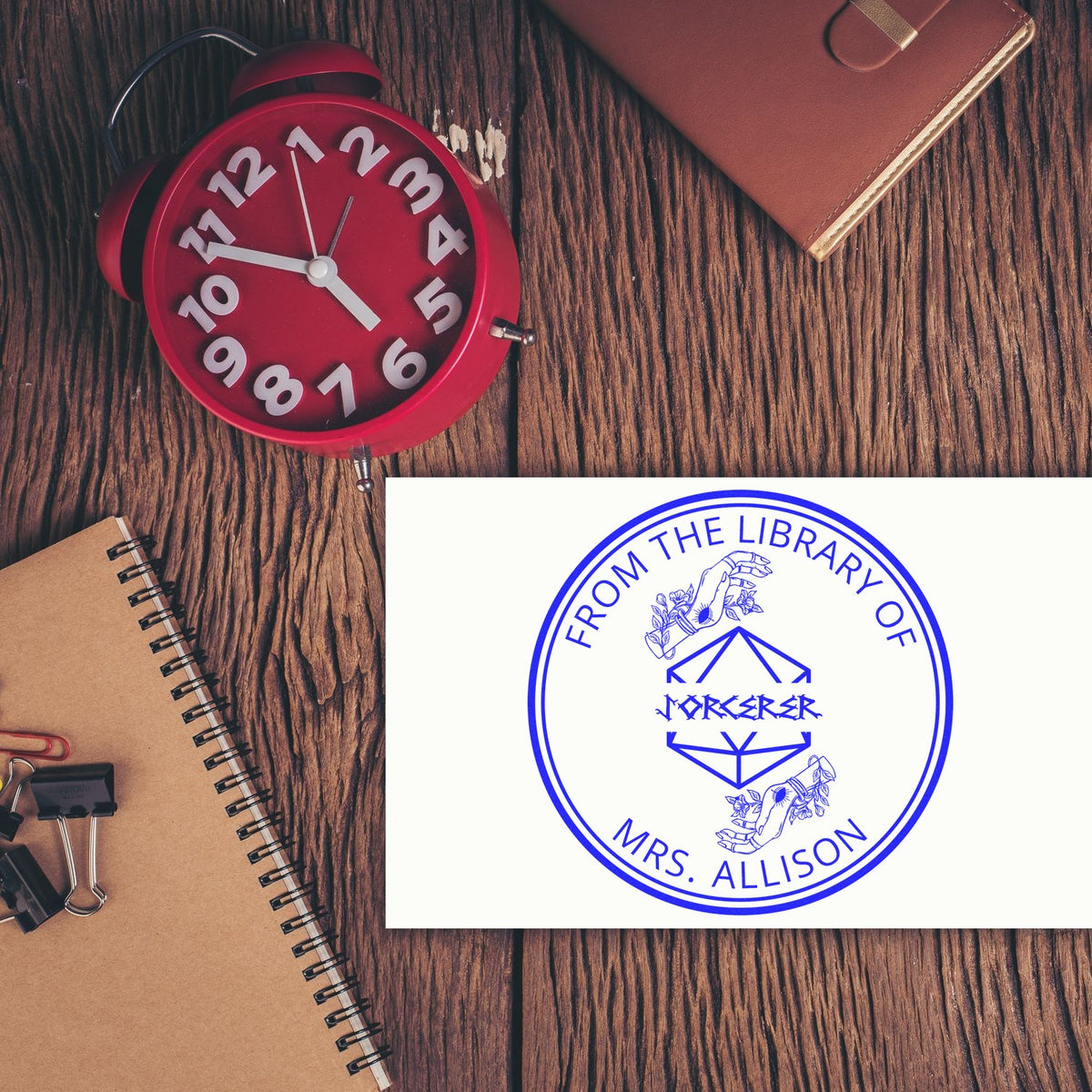 Red desk stamp and blue custom library seal on a wood-grain desk with notebook.