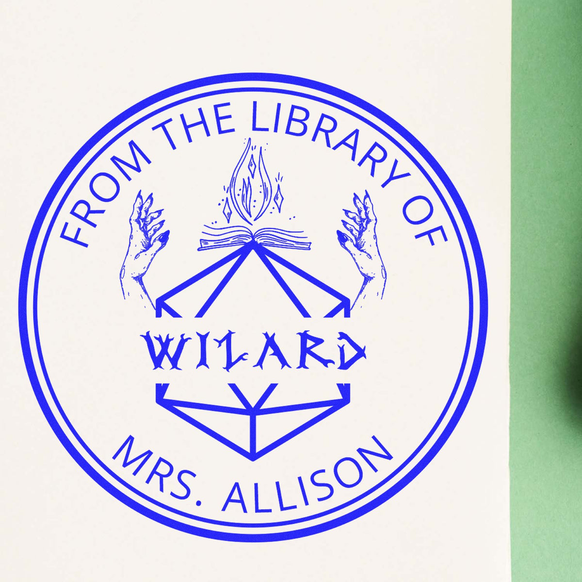 Blue circular library stamp seal with hands, open book and torch on white, bordered by green.