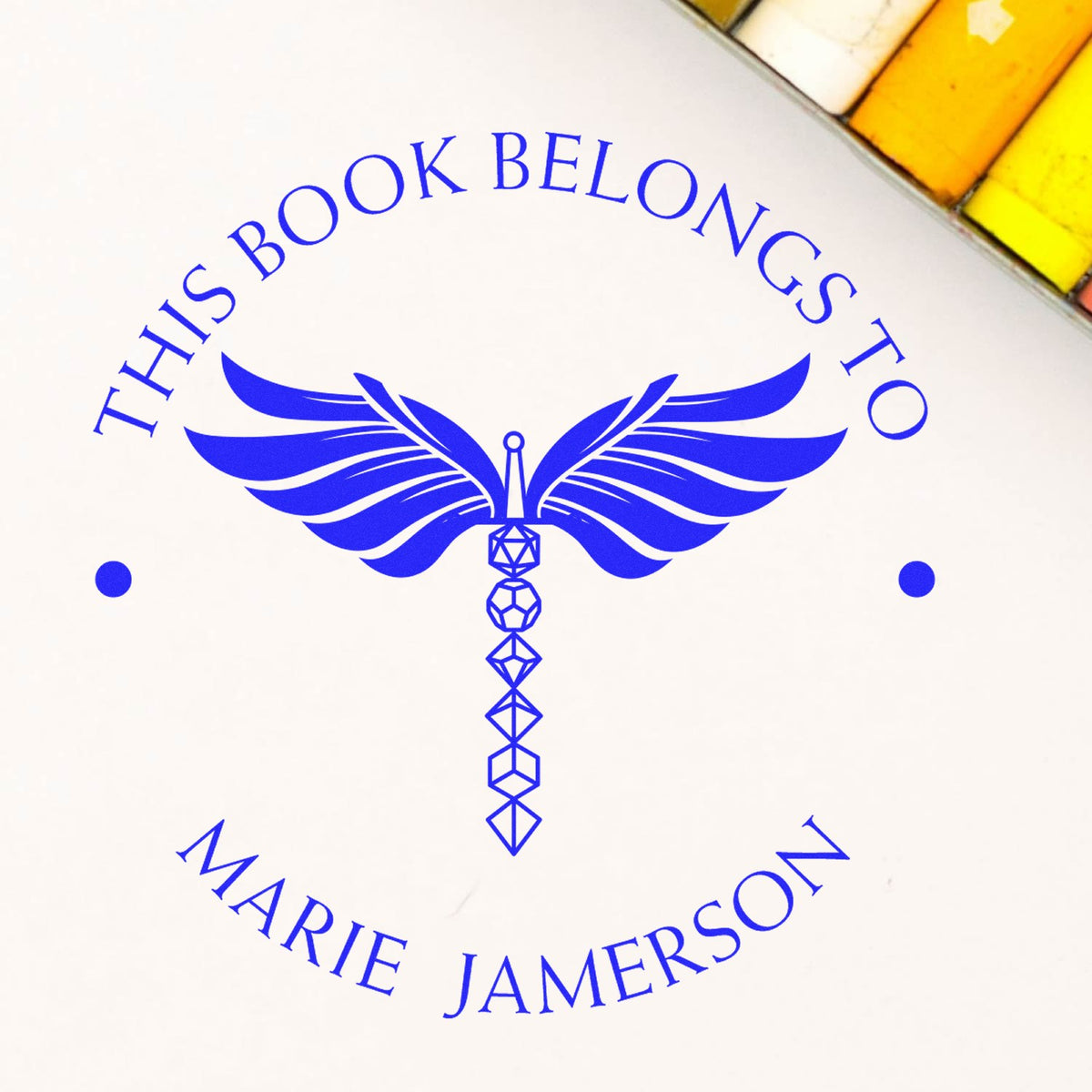 Blue personalized book seal stamp with winged wand emblem and text This Book Belongs to Marie Jamerson on white.