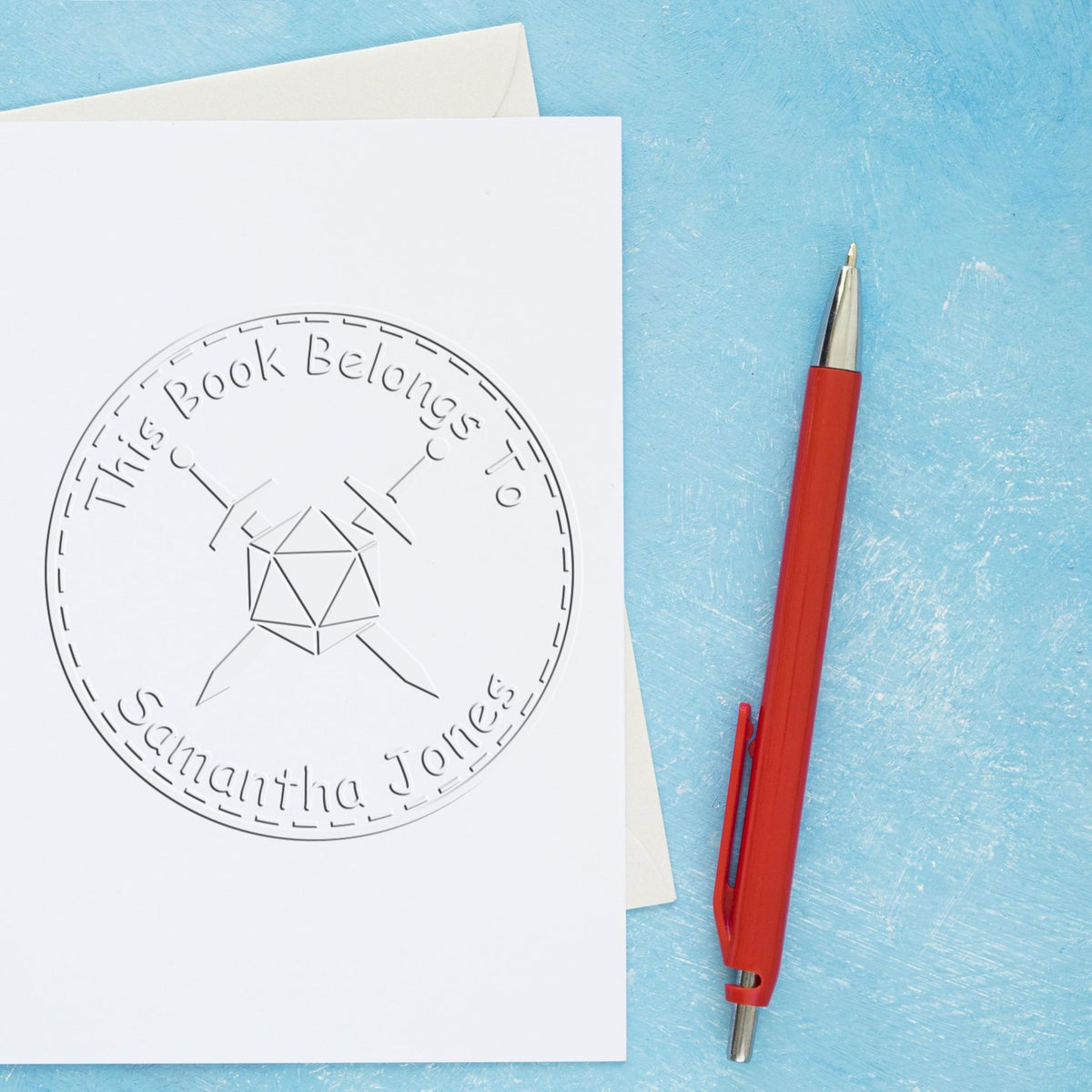 Embossed bookplate stamp seal on white card, with red pen on a pale blue background and envelope.