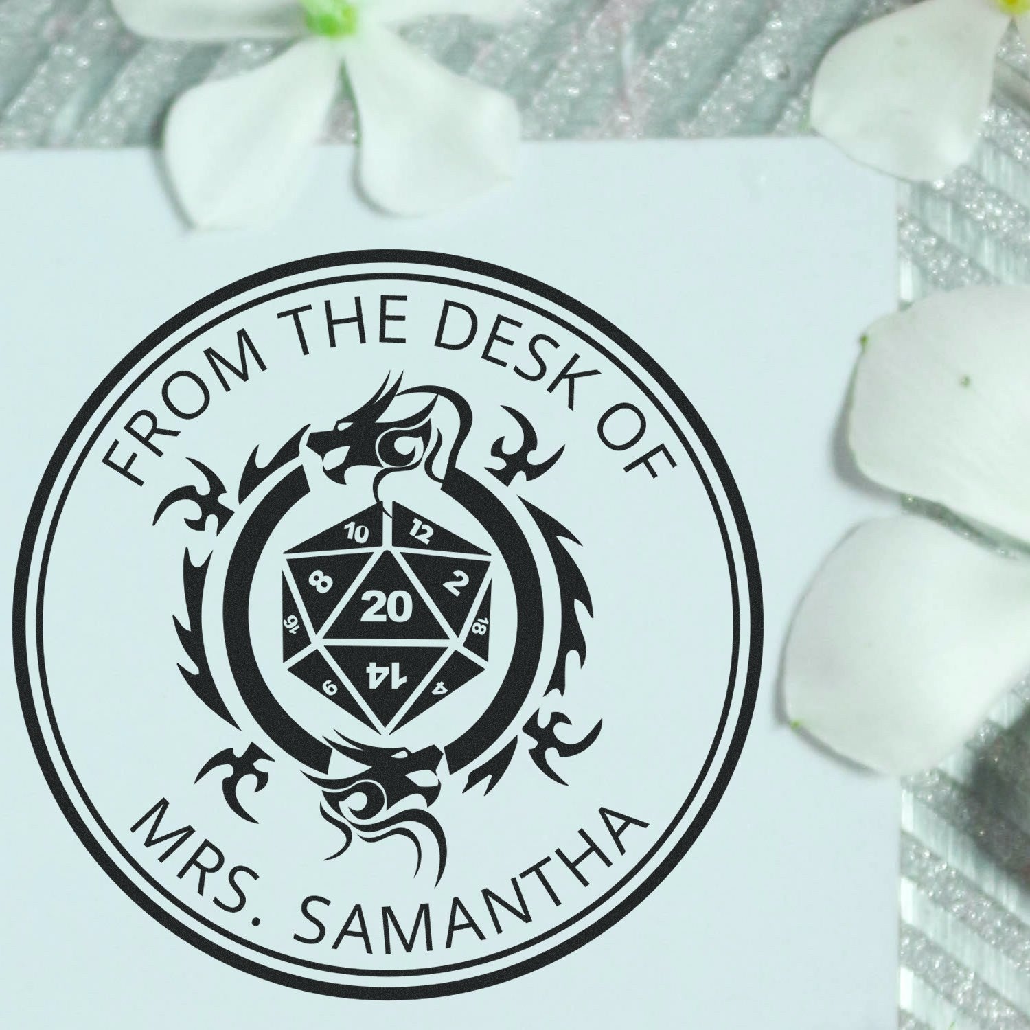 Black circular desk seal stamp on white card with dragon crest and D20 dice, reading From the Desk of Mrs. Samantha.