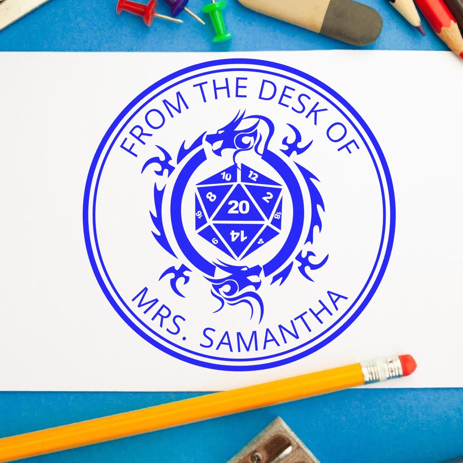 Blue custom desk stamp seal with dragon and From the Desk of Mrs. Samantha, on white paper with colored pencils.