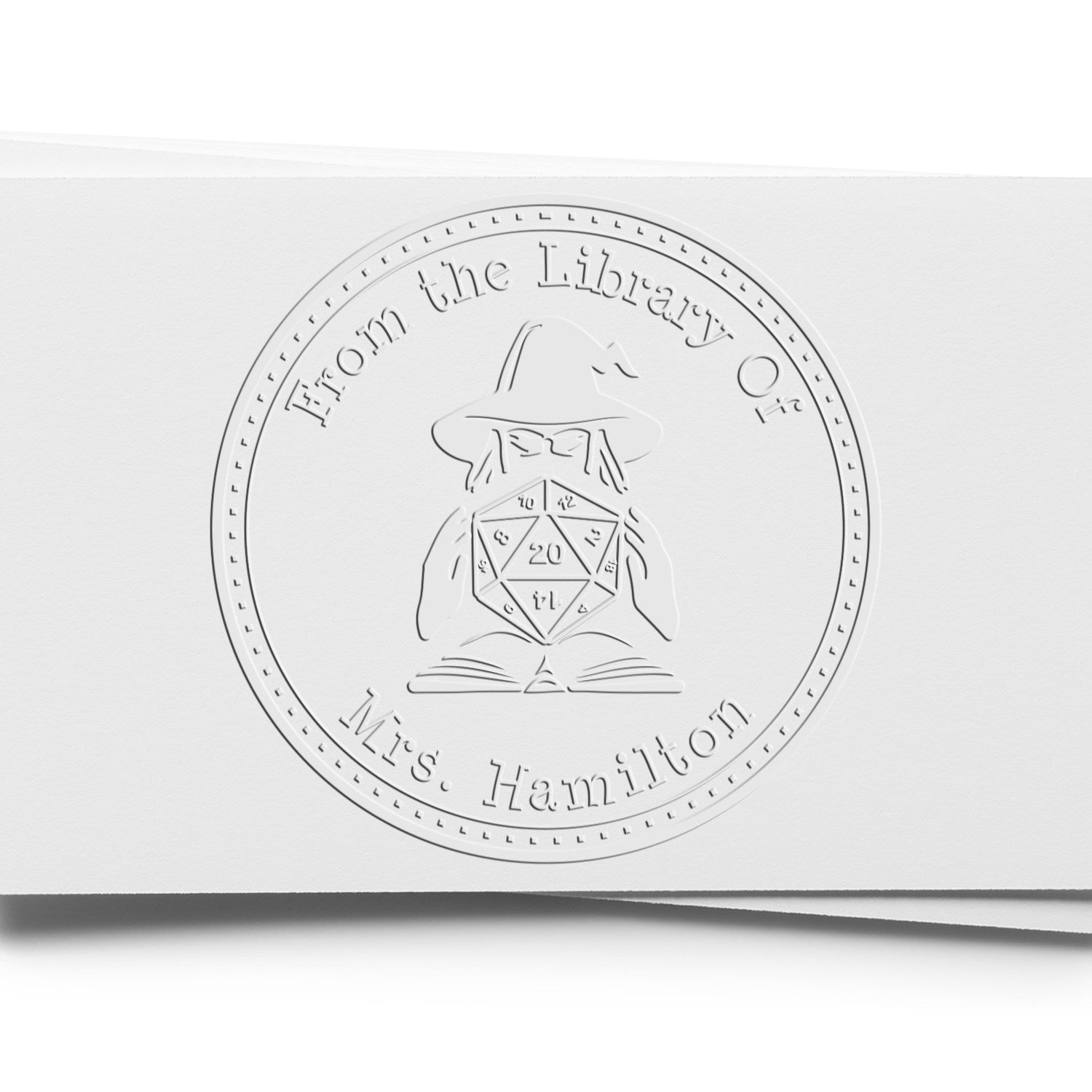 Embossed white circular stamp seal reading From the Library Of Mrs. Hamilton with a wizard and 20-sided die.