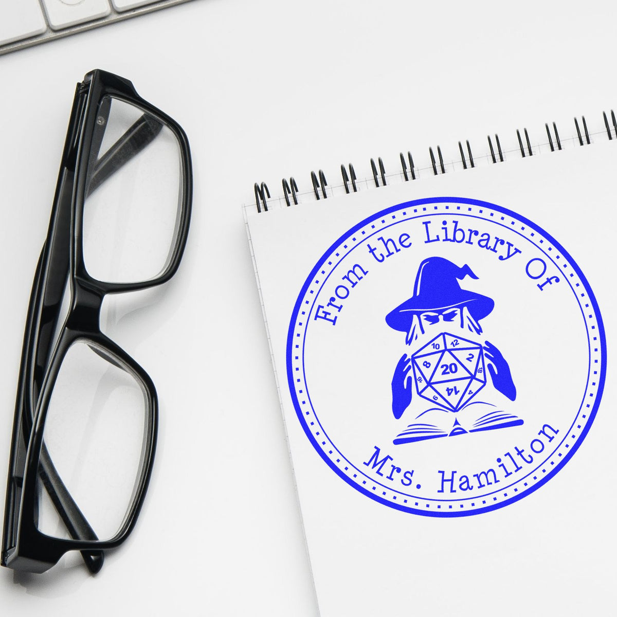 Black glasses beside a spiral notebook with a blue custom library stamp seal reading Mrs. Hamilton.