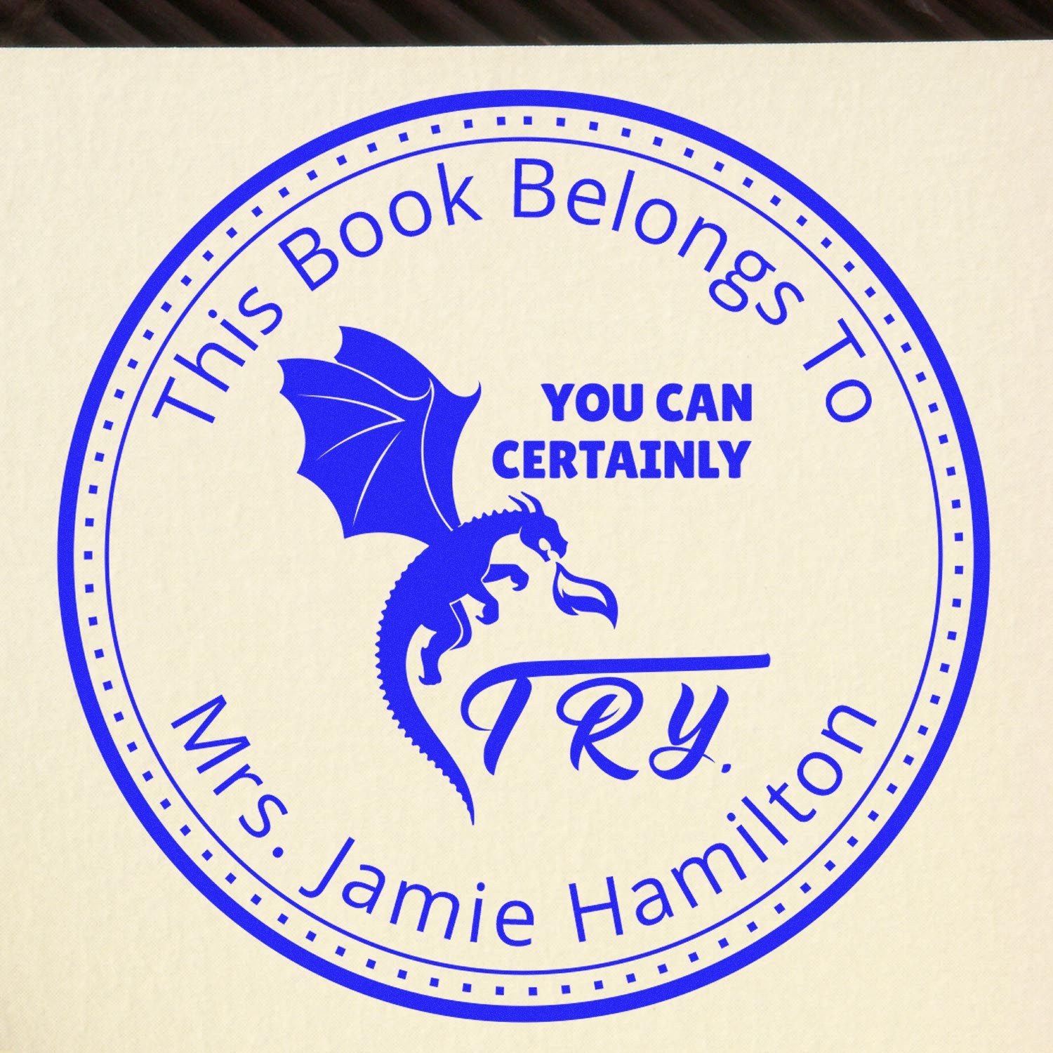 Blue circular stamp seal with dragon, You Can Certainly Try, and This Book Belongs to Mrs. Jamie Hamilton on cream background.