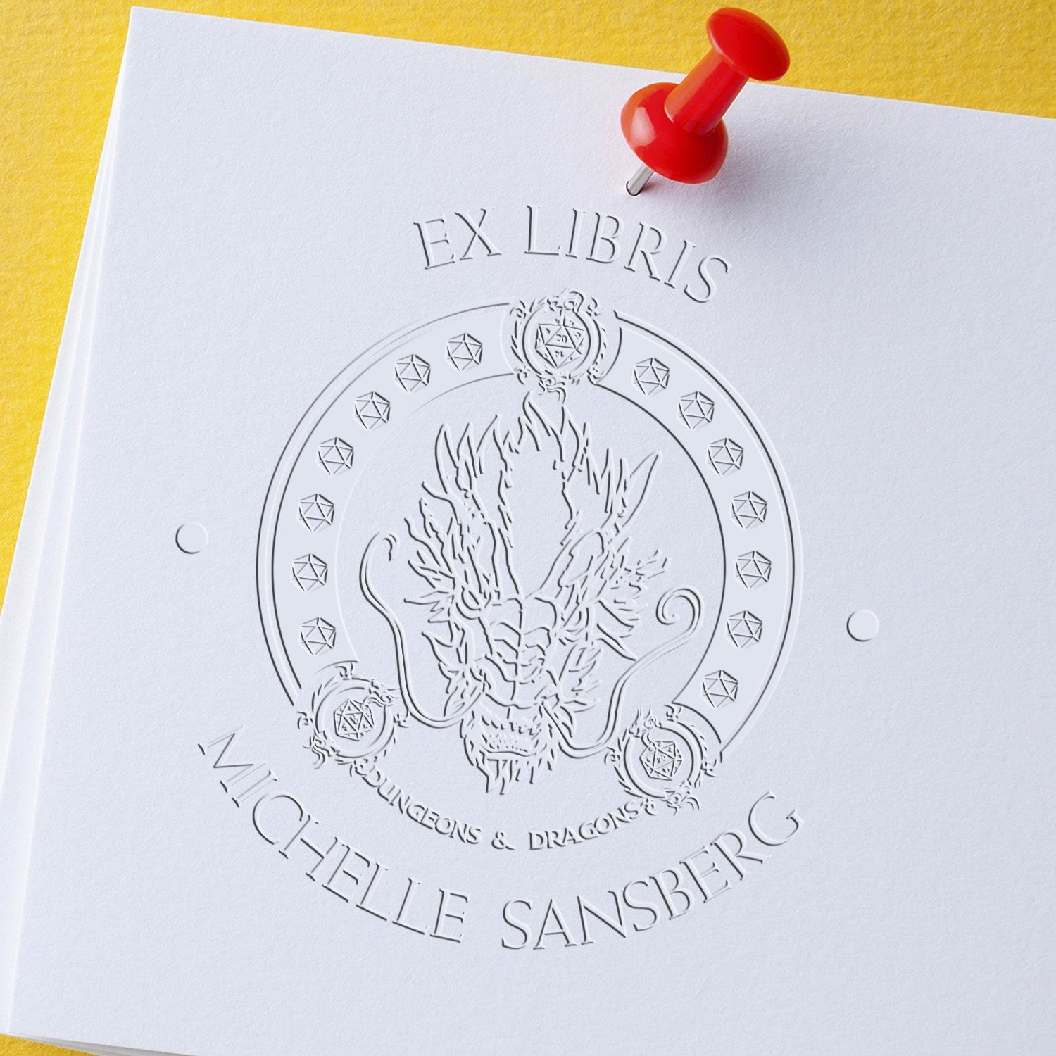 Embossed custom stamp and seal on white paper, showing “Ex Libris Michelle Sansberg” and a dragon crest, pinned with a red pushpin.