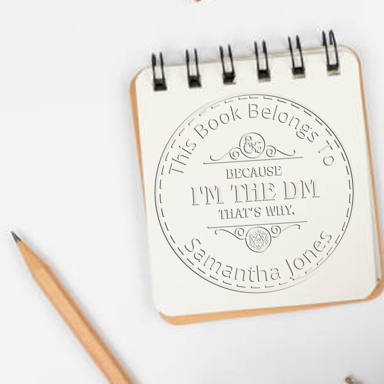 Cream spiral notebook with pencil and circular custom stamp seal reading This Book Belongs to Samantha Jones.
