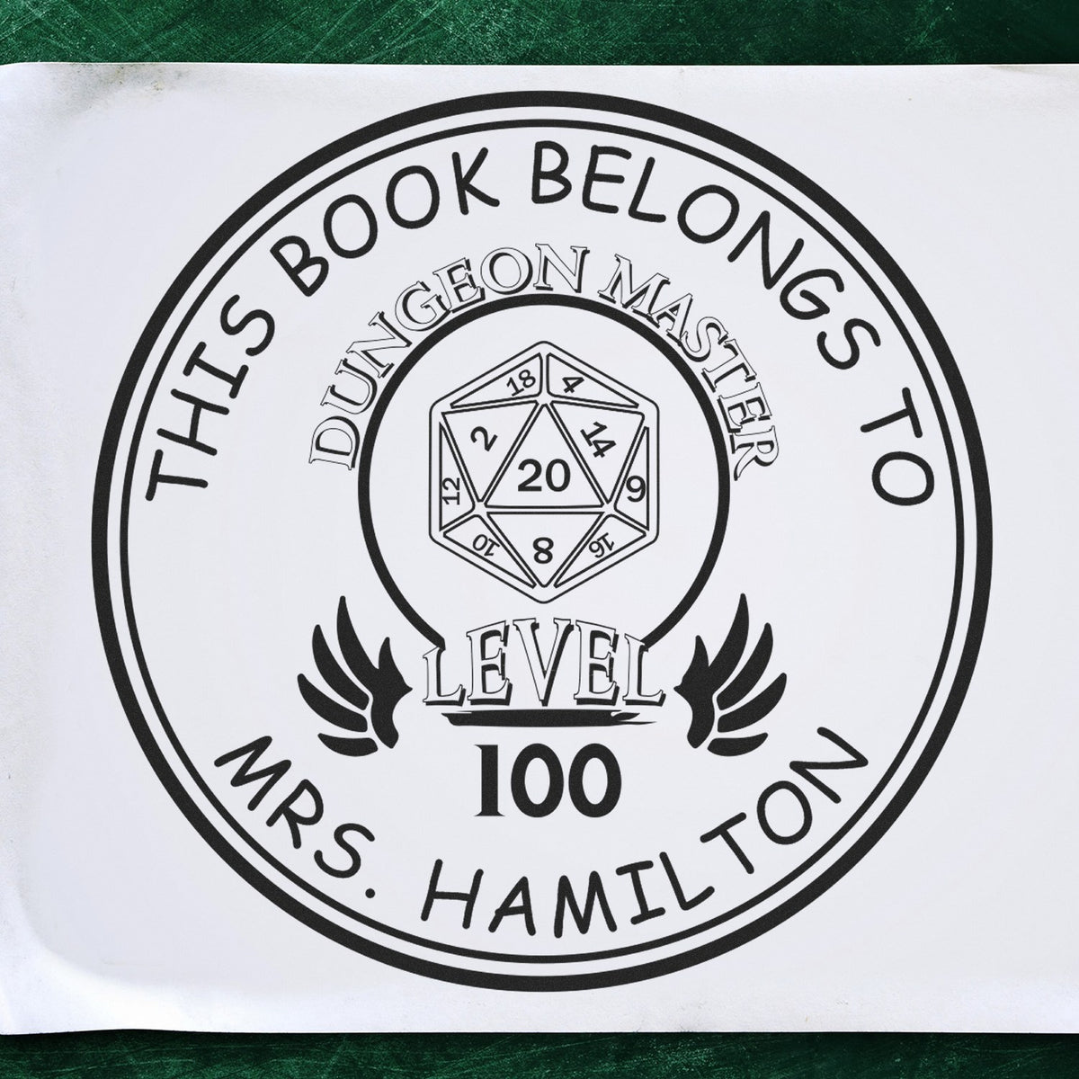 Round stamp design with 'This Book Belongs To' text, featuring a D20 dice and 'Dungeon Master Level 100' in the center. Includes 'Mrs. Hamilton' at the bottom. Keywords: WhiskerTwist Cartoon Animal Pre-Inked Customizable Library Ownership Stamp, Personalizable Address Stamp.